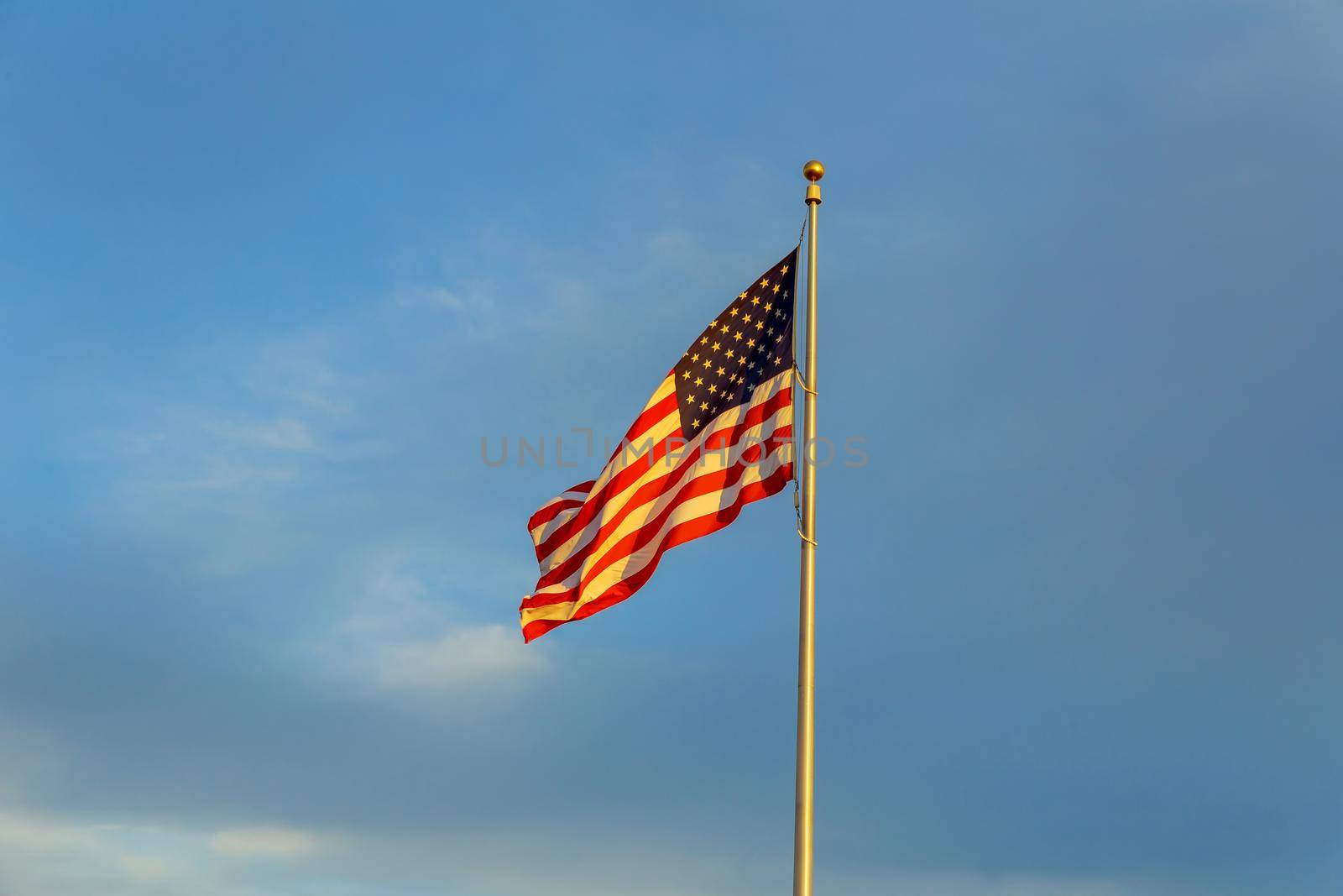 American flag flagpole waving in the wind against clouds, blue sky