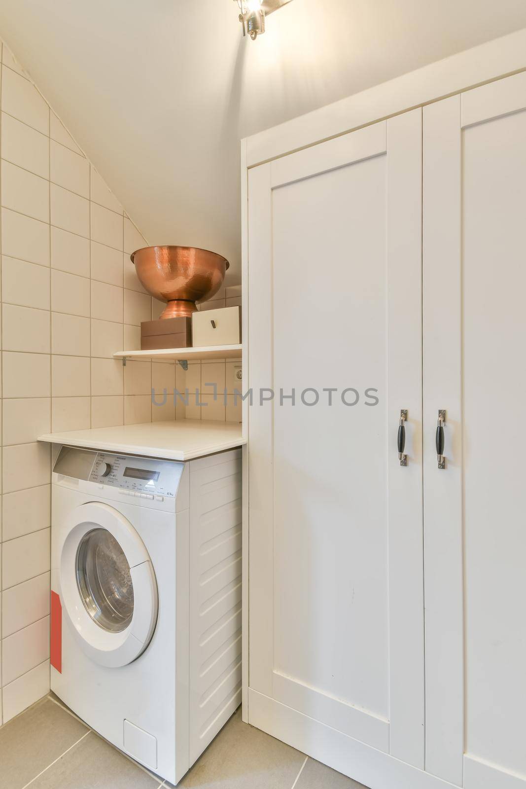 The interior of a laundry room with a washing machine and a white wardrobe in a modern house