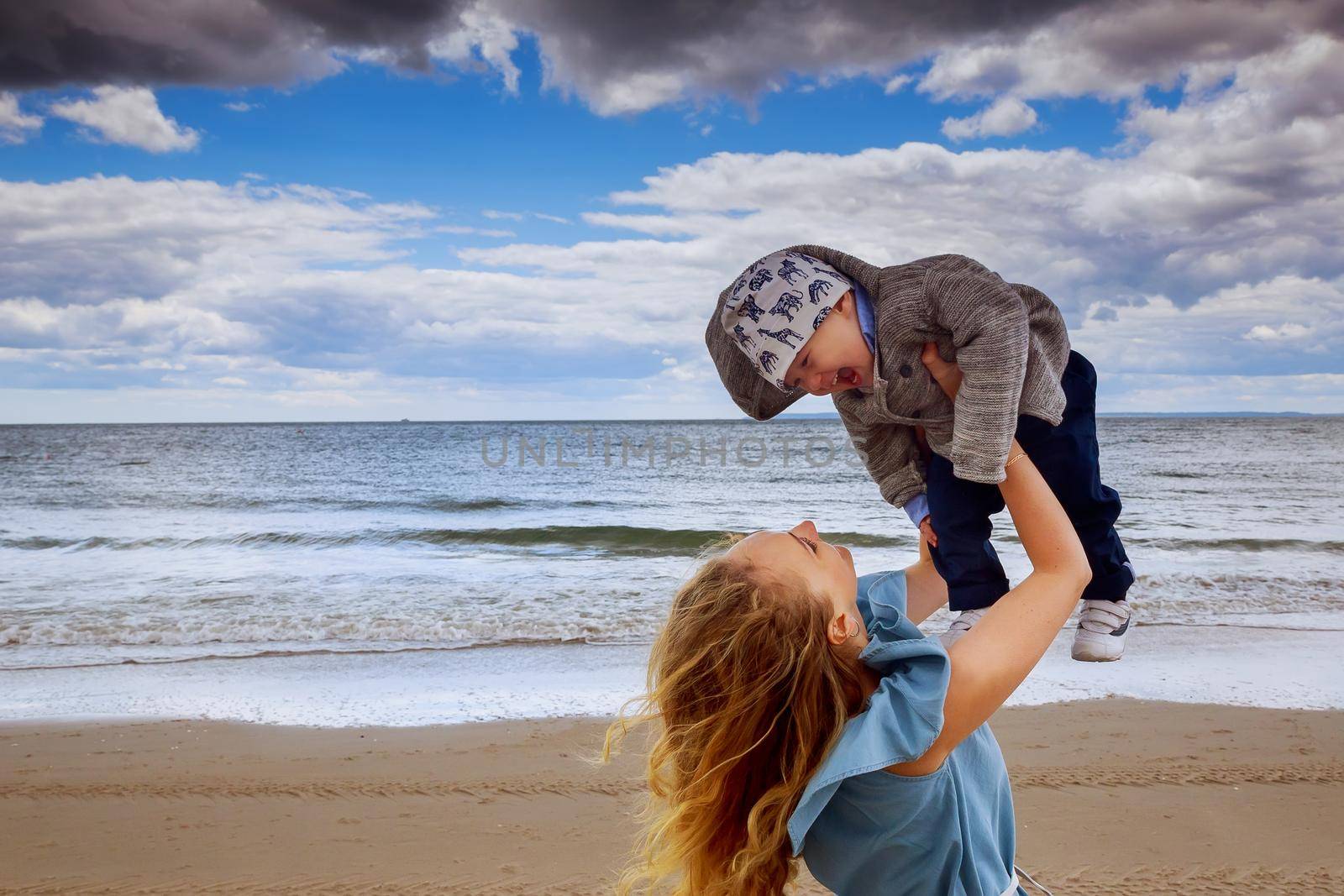 Happy family. Young mother throws up baby in the sky, on sunny day. Portrait mother and little son on the beach. by ungvar