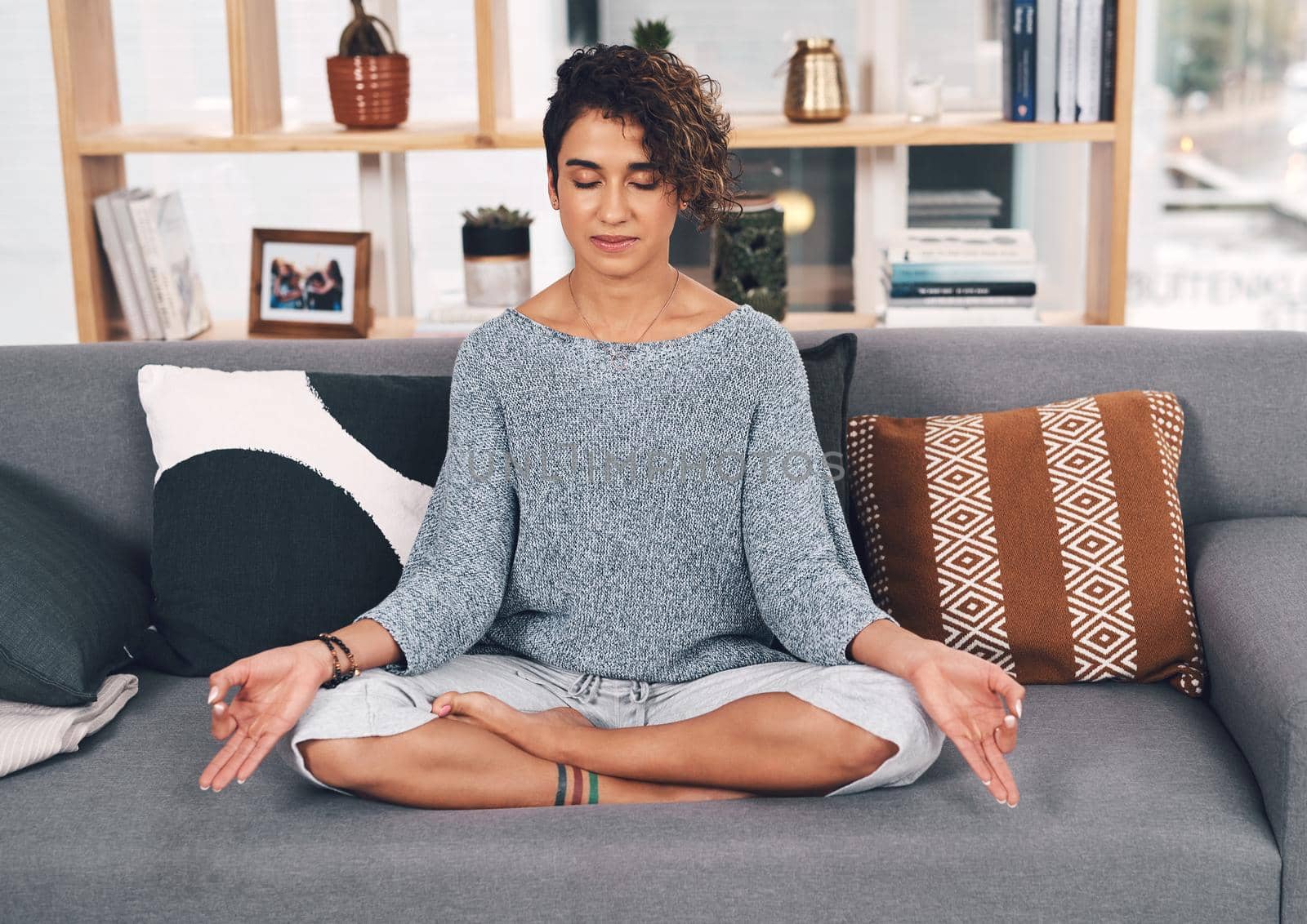 Full length shot of an attractive young woman sitting and meditating on her sofa in the living room at home.