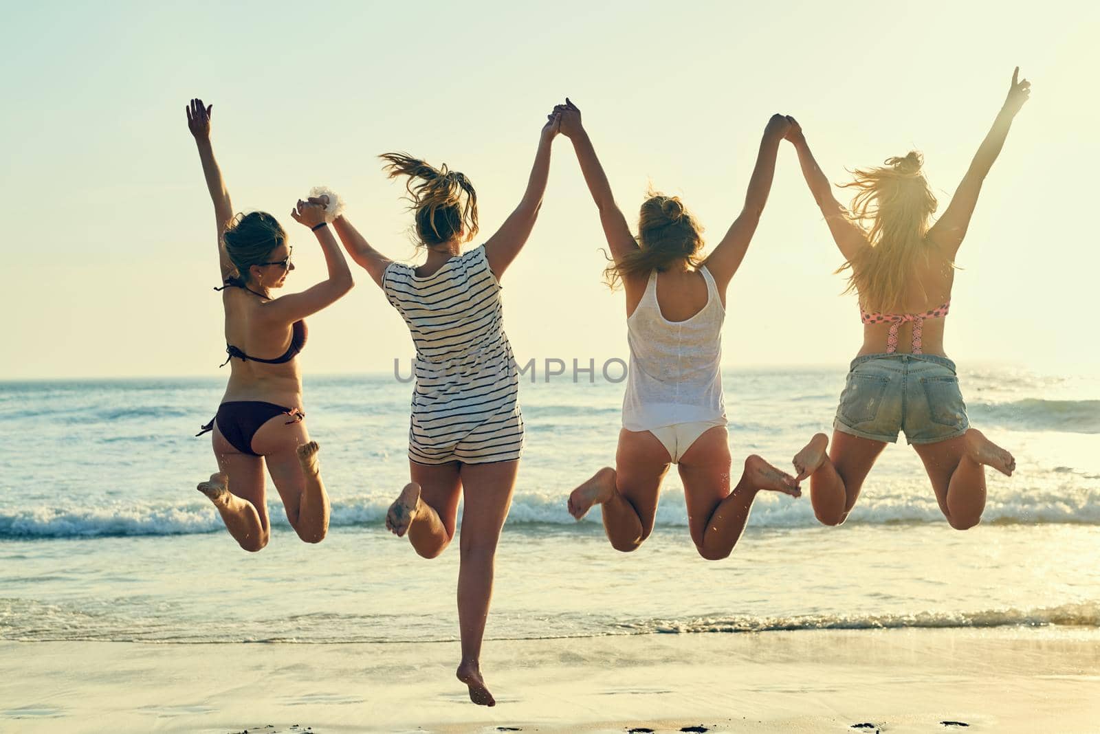 Beach days are the best days. Rearview shot of female best friends jumping in the air at the beach. by YuriArcurs