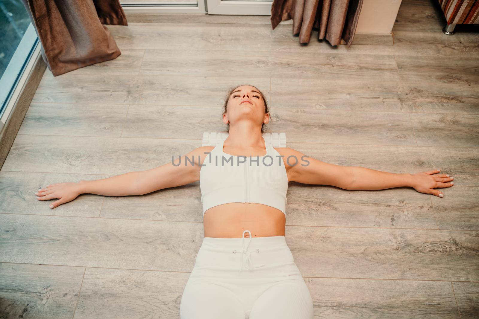 Adult athletic woman, in white bodysuit, performing fascia exercises on the floor - caucasian woman using a massage foam roller - a tool to relieve tension in the back and relieve muscle pain - the concept of physiotherapy and stretching training by Matiunina