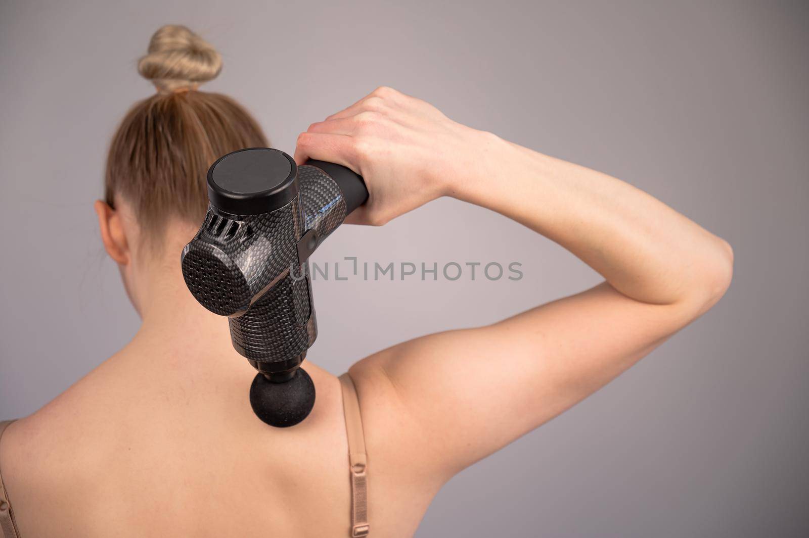 Caucasian woman giving herself a back massage with a gun