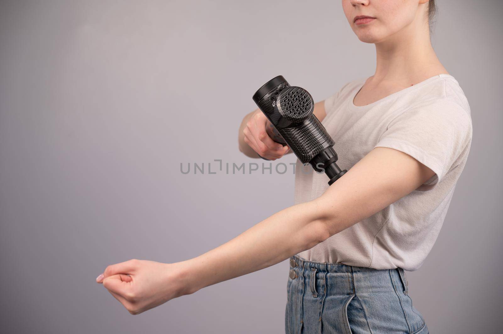 Caucasian woman uses a massager gun for pain in the muscles of the arm. by mrwed54