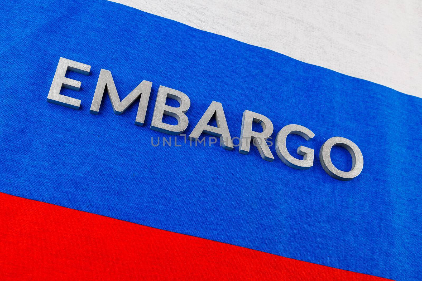 the word embargo laid with silver metal letters on russian tricolor flag in diagonal perspective view