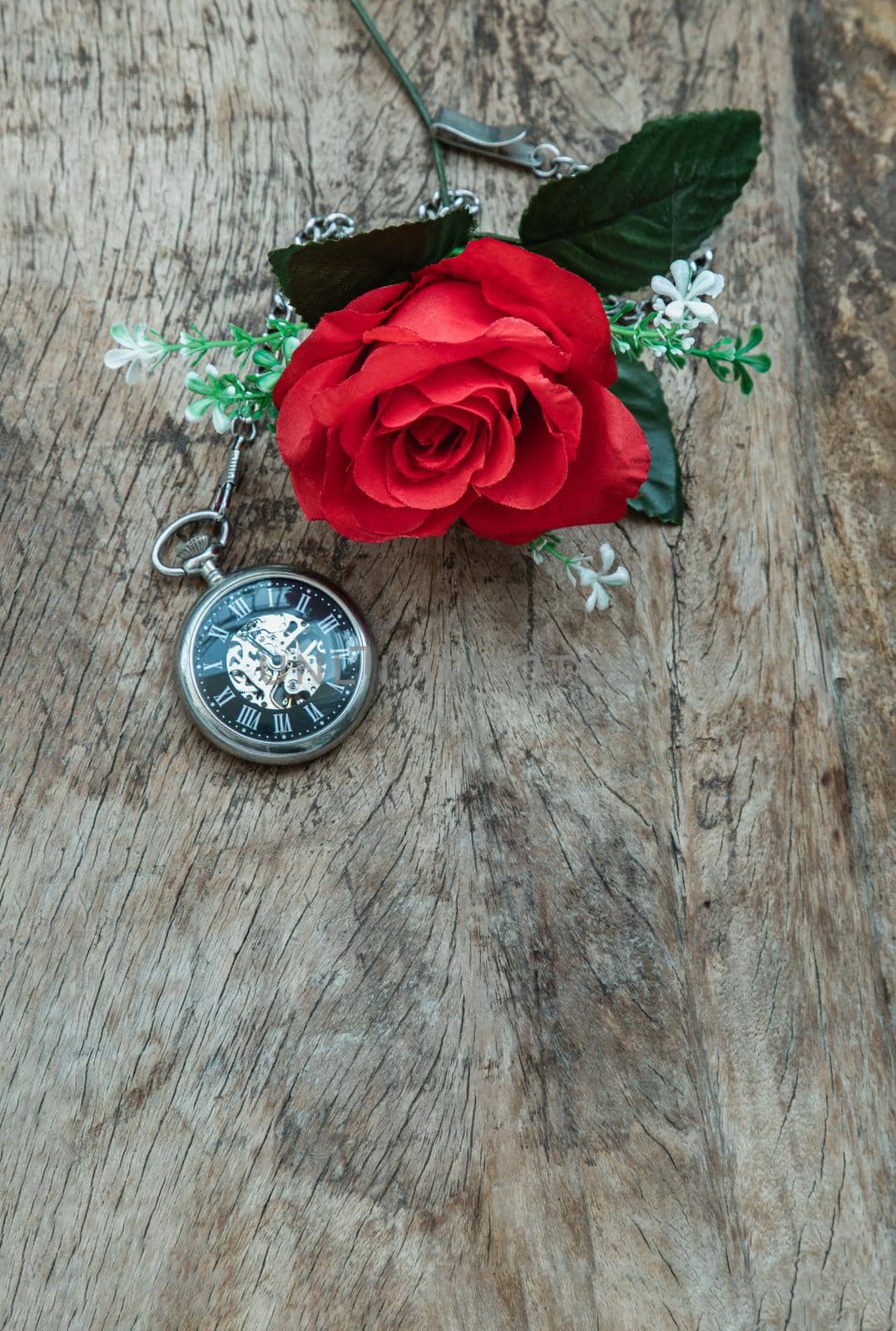 Red rose flower and A retro pocket watch on old wooden board background.  by tosirikul