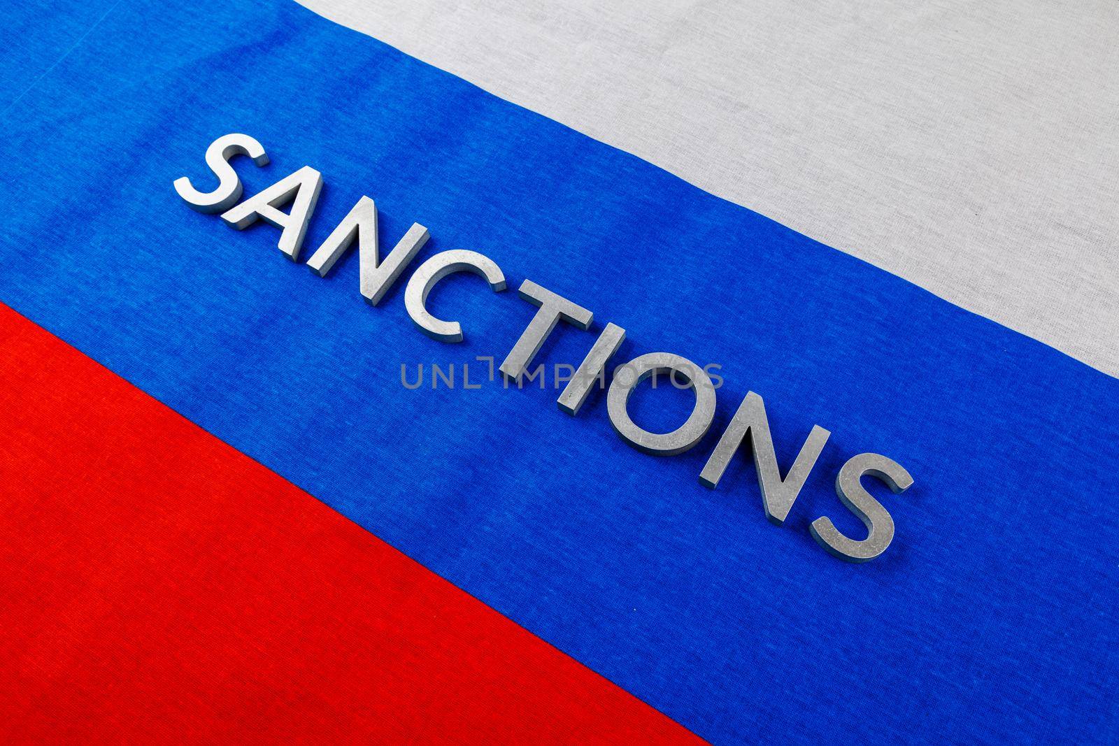 the word sanctions laid with silver metal letters on russian tricolor flag in diagonal linear perspective