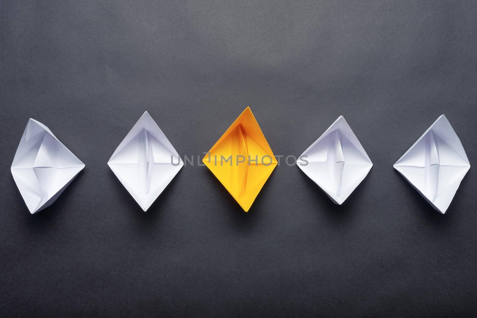 Row of paper ships on black background. Business concept of creative innovation and leadership. Flat lay yellow origami boat in group of white boats. Social marketing layout with copy space.