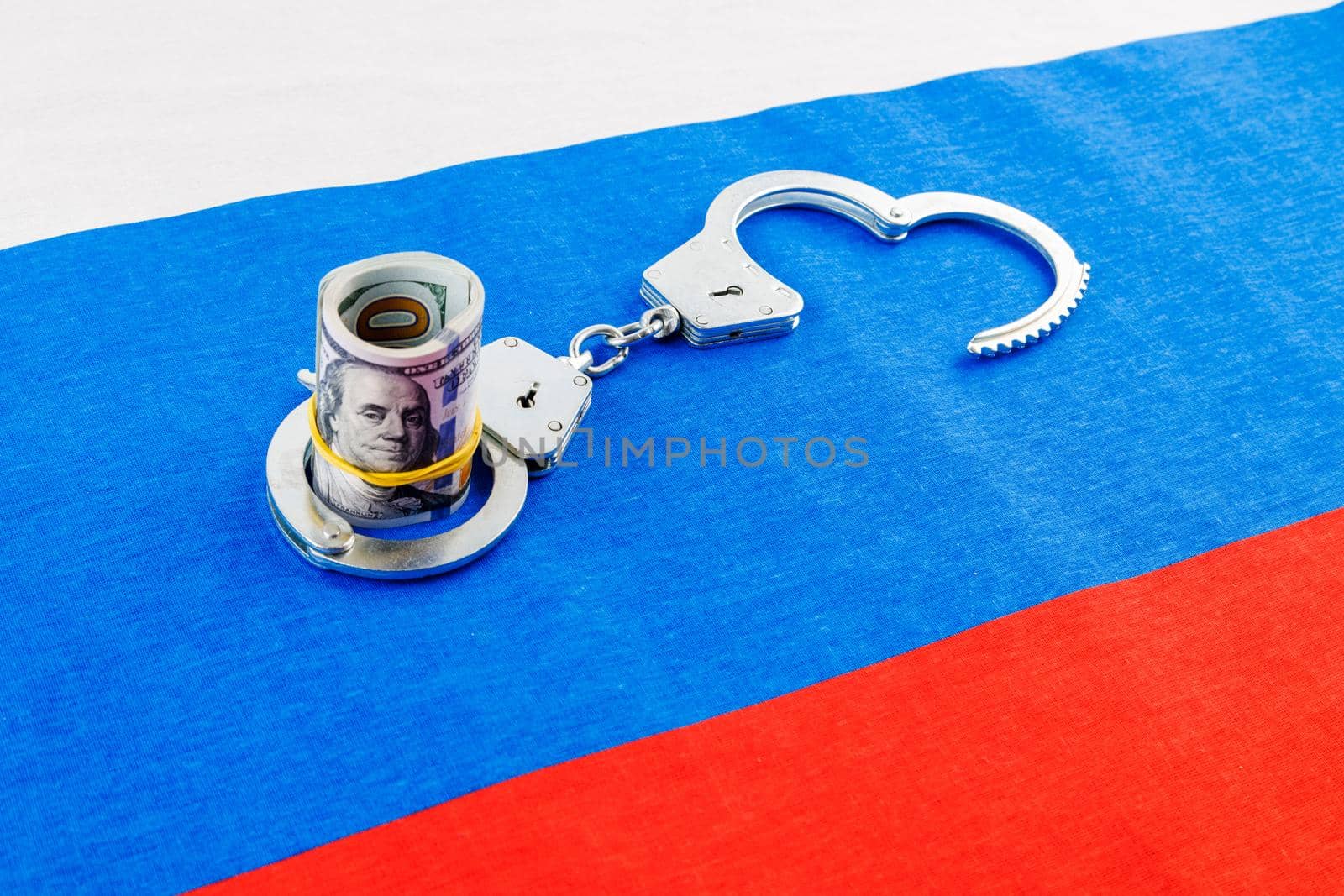 roll of us dollar banknotes in a handcuffs on flat full-frame russian flag, closeup