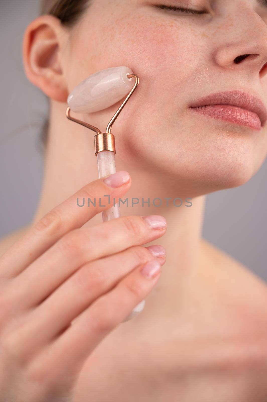 Close-up portrait of a woman using a quartz roller massager on her cheek for an alternative anti-aging