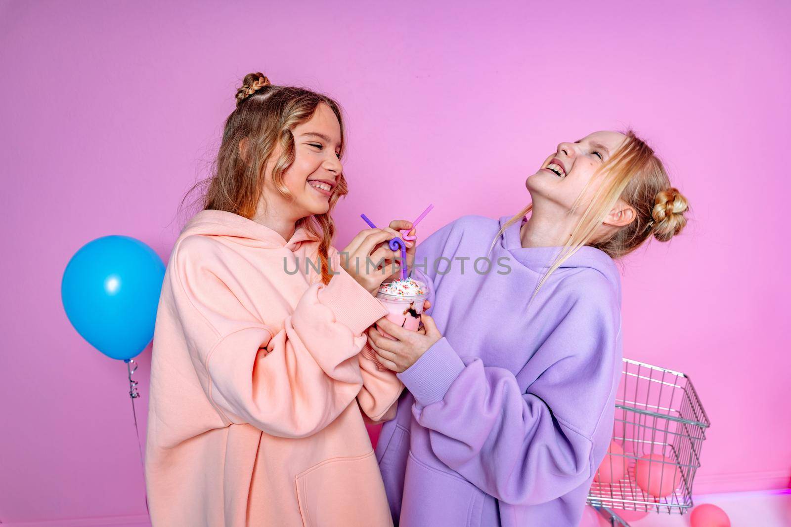 Two beautiful attractive funny joyful cheerful relaxed carefree girls dressed in casual fashion clothes isolated on hot pink background by Matiunina