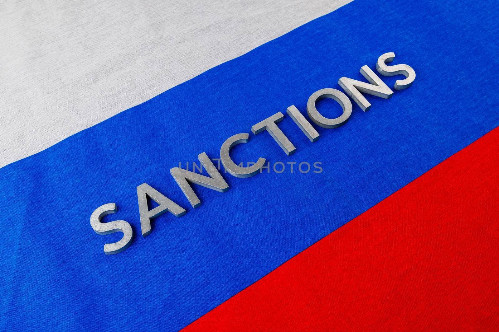 the word sanctions laid with silver metal letters on russian tricolor flag in diagonal linear perspective