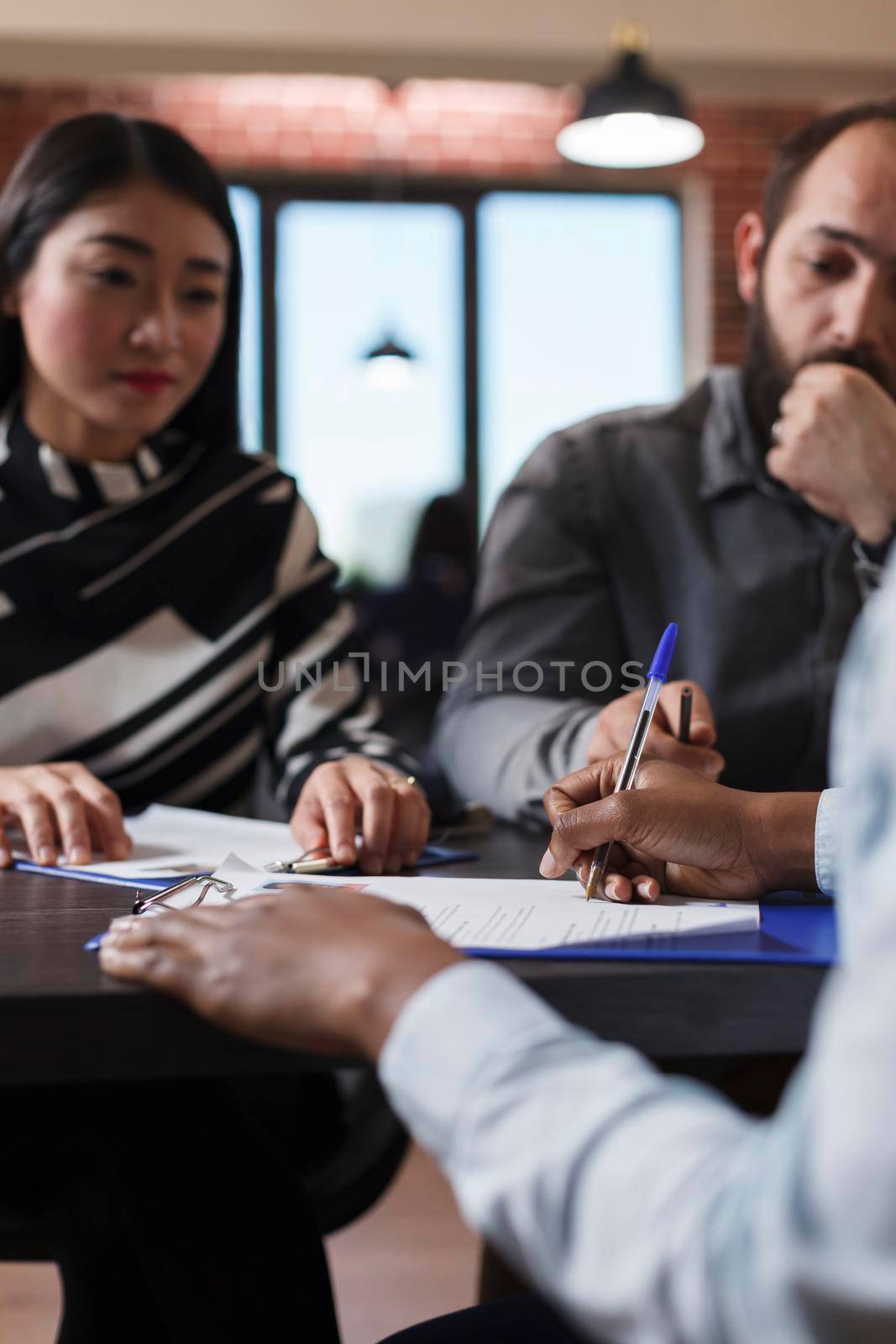 African american woman completing employment form and internal regulations while sitting at desk with recruitment team. Multi ethnic recruiters sitting in office while instructing future employee.