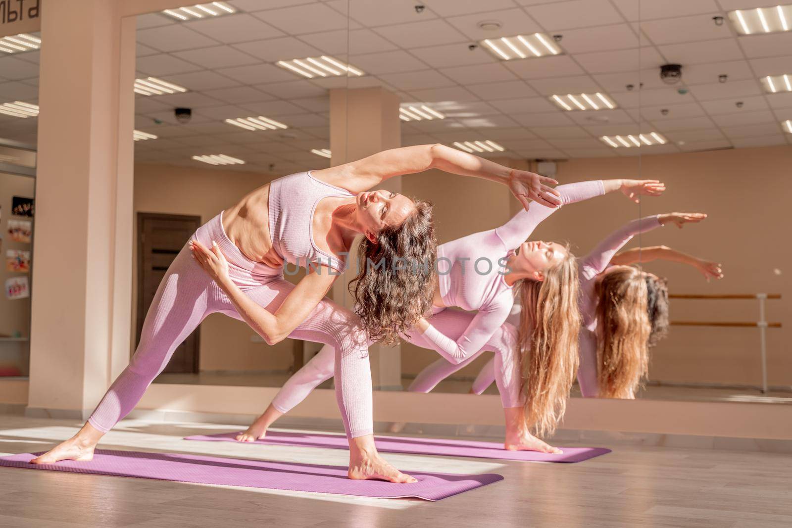 Two beautiful women cook doing yoga, sports together in the gym. Dressed in pink suits. The concept of grace and beauty of the body