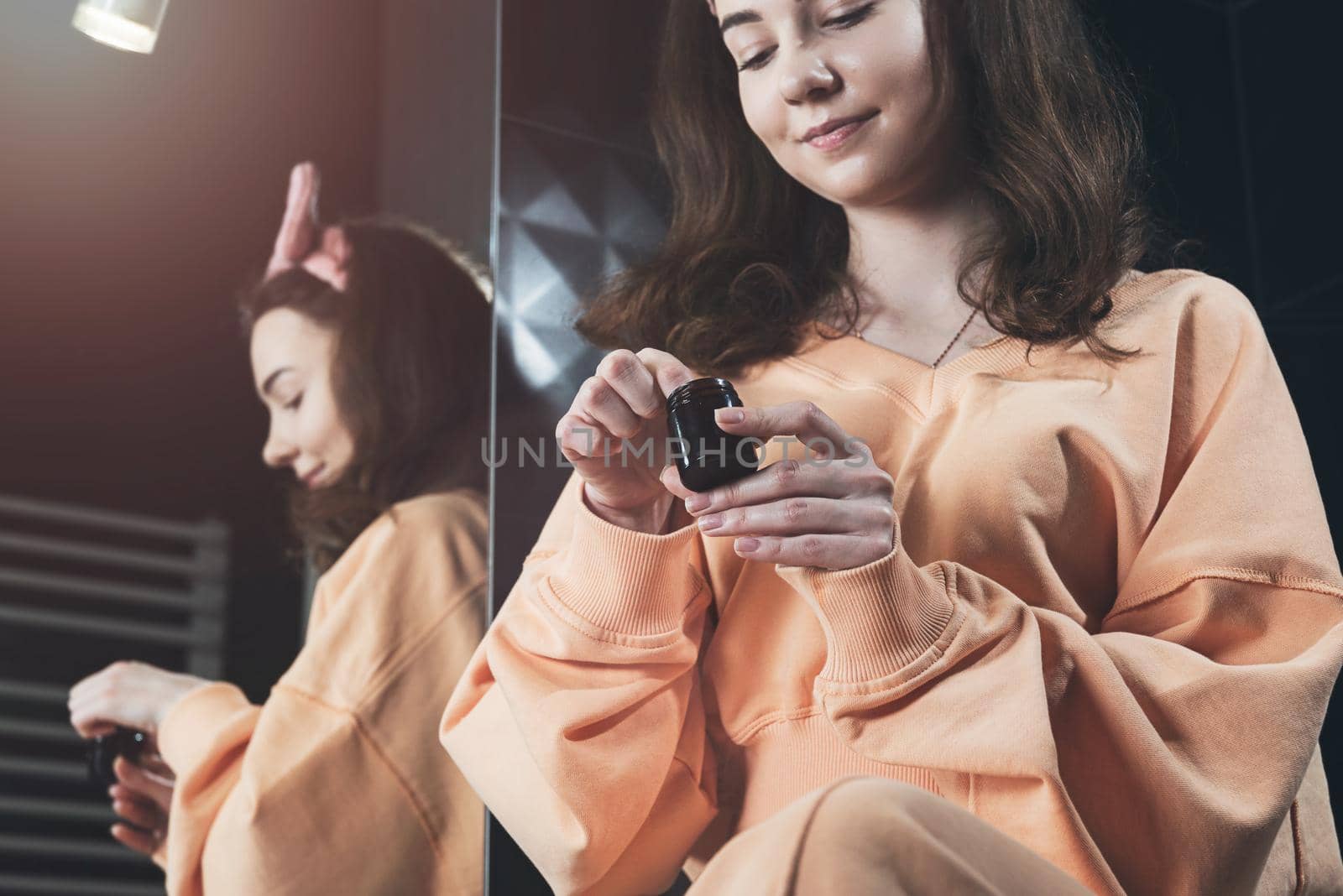 Woman is holding an open jar of cream and applies a small amount of the product to her hand. Concept of skin care, testing and selection of high-quality natural and organic cosmetics. Closeup