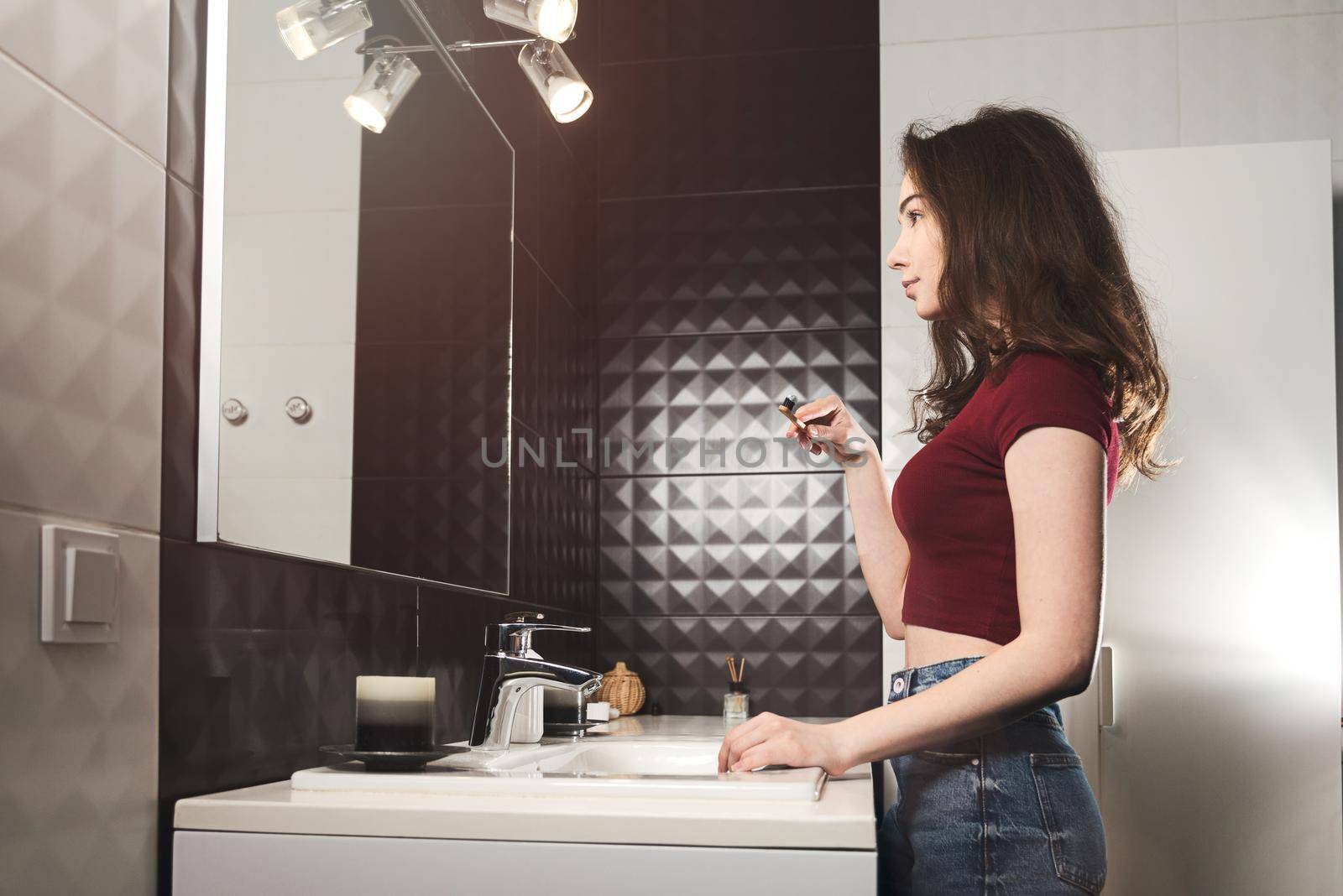 Woman brushing her teeth. Young woman in a burgundy top and jeanse with bamboo brush in front of the mirror. by Ashtray25
