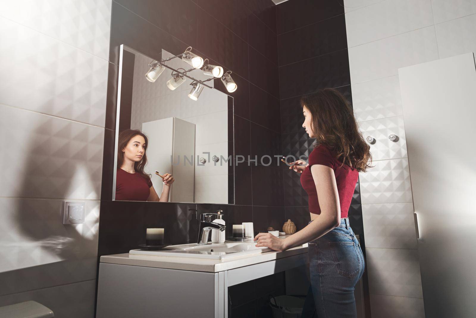 Woman brushing her teeth. Young woman in a burgundy top and jeanse with bamboo brush in front of the mirror. by Ashtray25