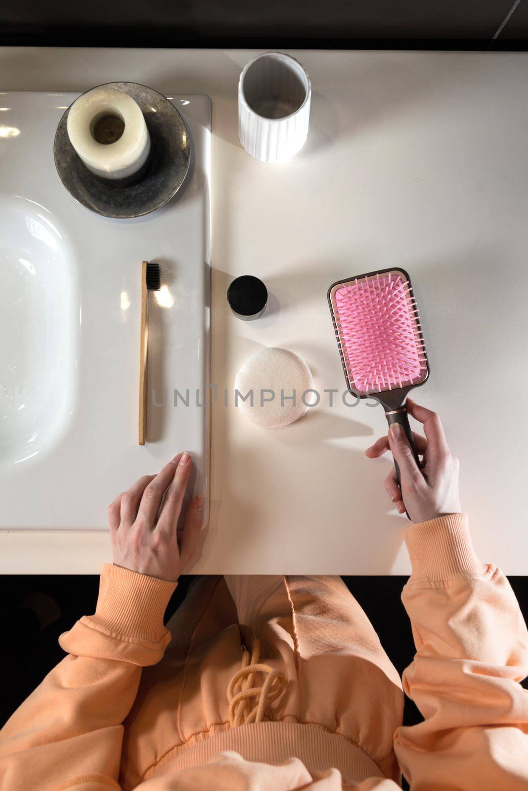 top view of bathroom accessories, toothbrush near hair brush, bow, mobile phone and face sponge on a white surface.