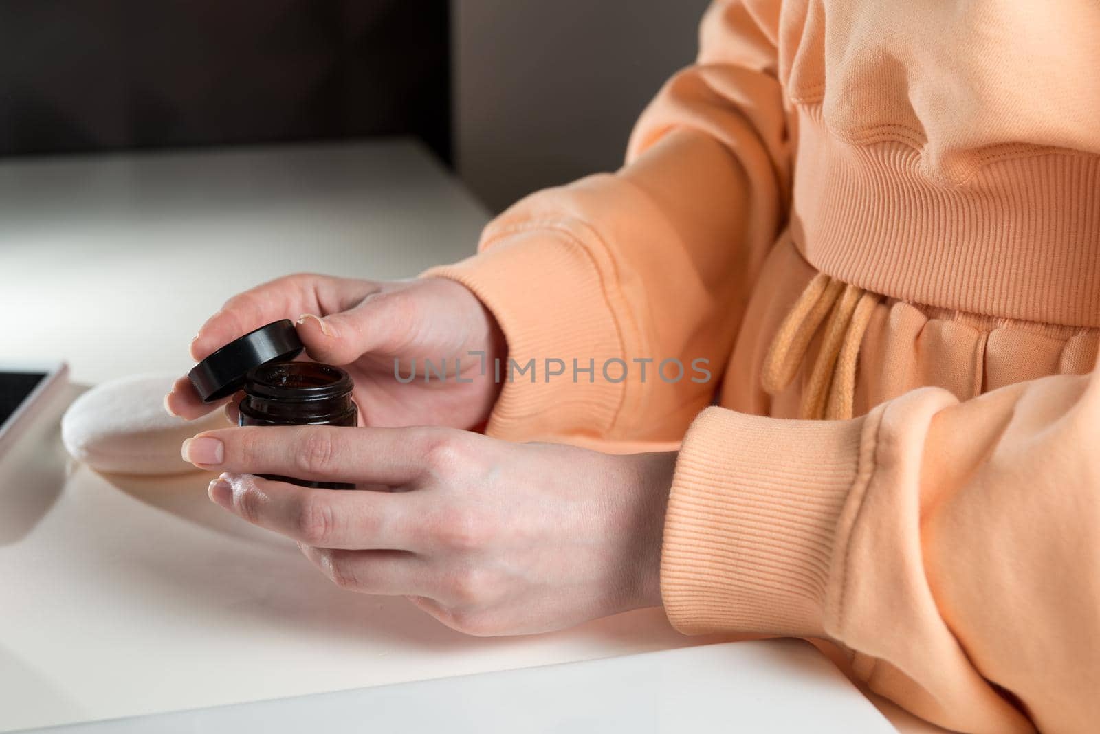 Woman is holding an open jar of cream and applies a small amount of the product to her hand. Concept of skin care, testing and selection of high-quality natural and organic cosmetics. Closeup