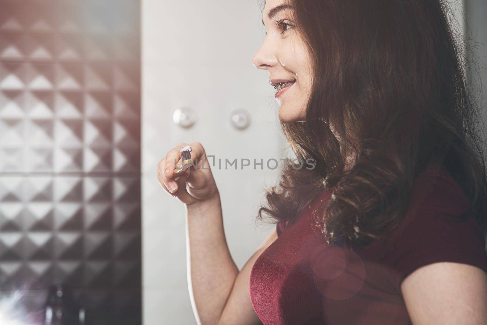 Woman brushing her teeth. Young woman in a burgundy top with bamboo brush. Bathroom with a black tiles