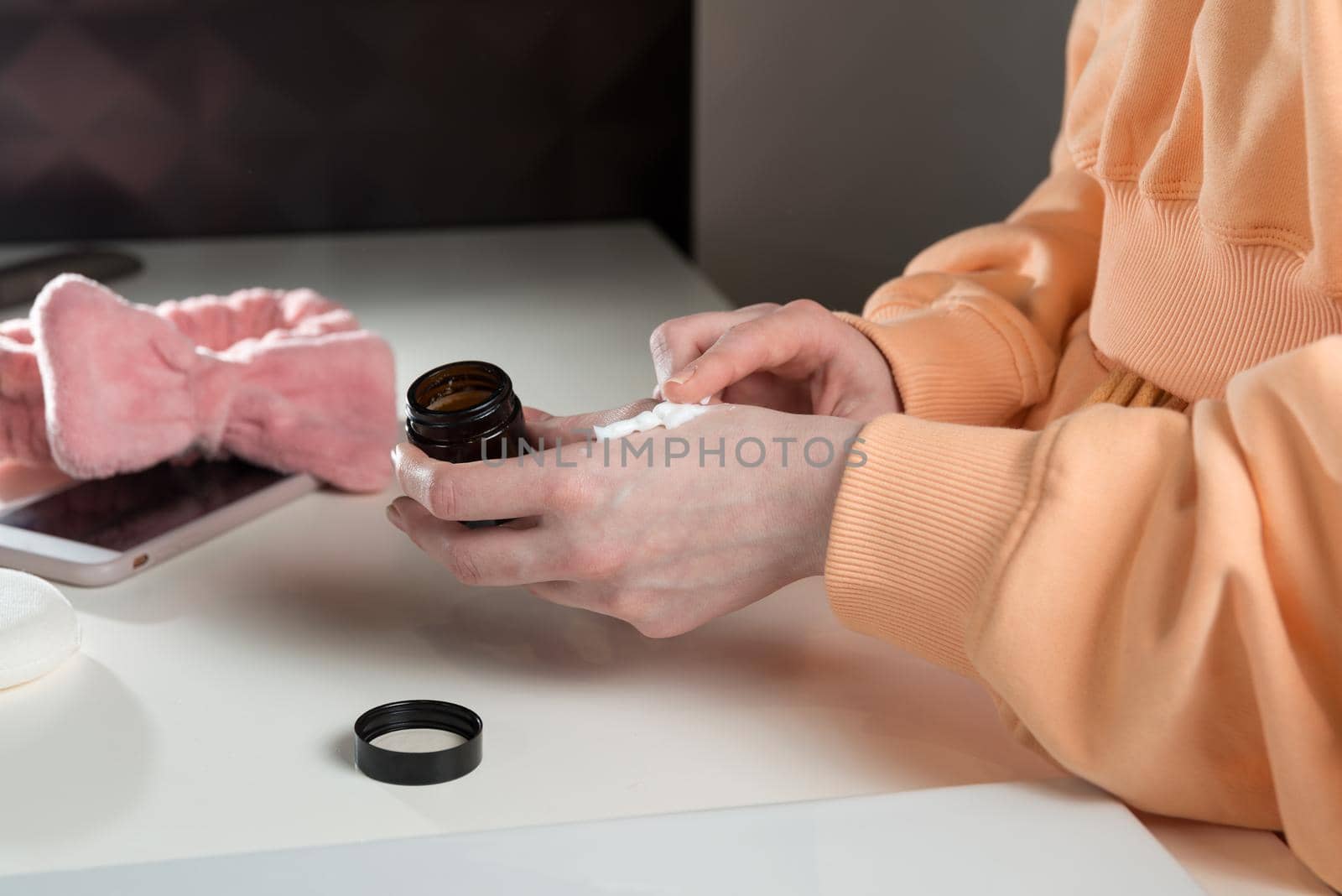 Woman is holding an open jar of cream and applies a small amount of the product to her hand. by Ashtray25