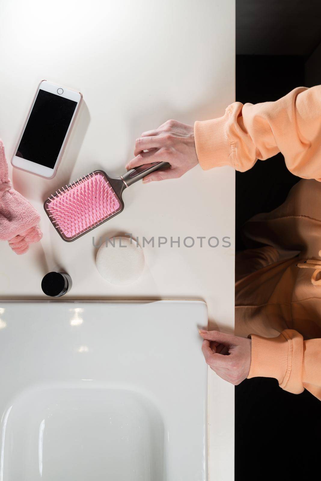 top view of bathroom accessories, toothbrush near hair brush, bow, mobile phone and face sponge on a white surface.