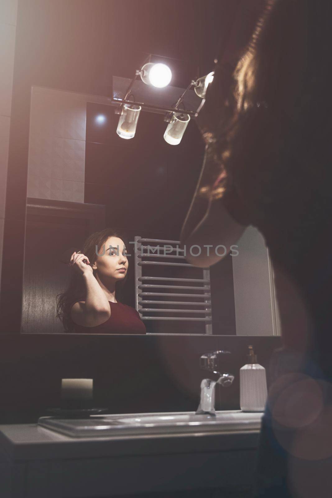 Young woman brushing hair in front of a bathroom mirror. by Ashtray25