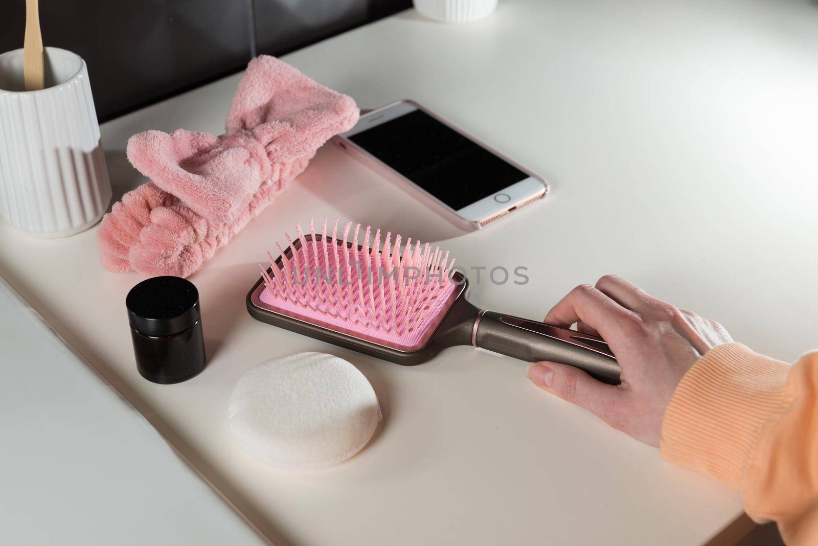 top view of bathroom accessories, toothbrush near hair brush, bow, mobile phone and face sponge on a white surface.