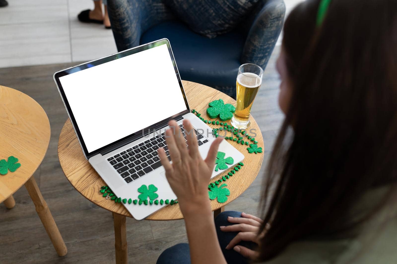 Caucasian woman holding beer on st patrick's day laptop video call with copy space on screen. fun during celebration of the irish patron saint's day.