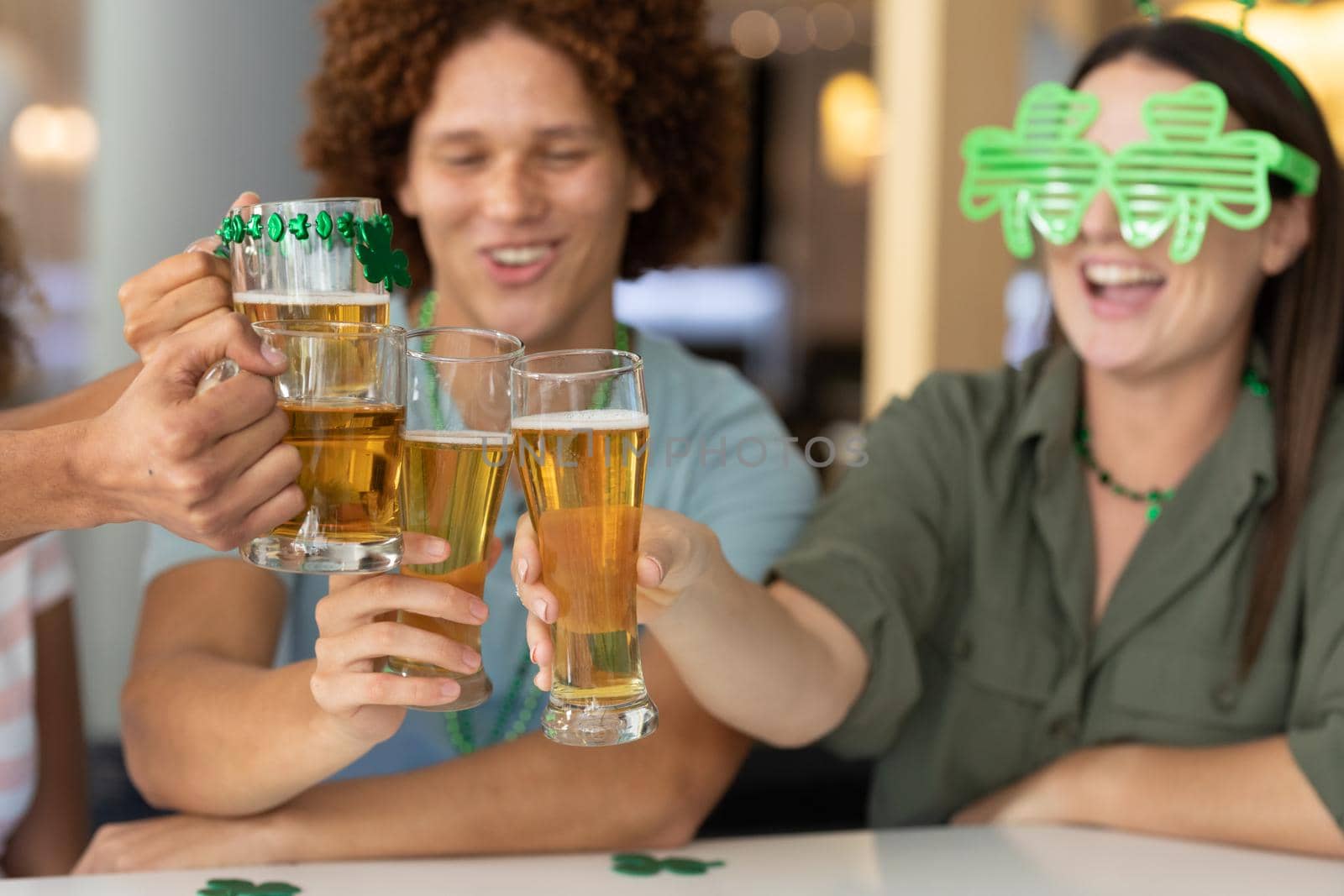 Diverse group of happy friends celebrating st patrick's day making toast with glasses of beer at bar by Wavebreakmedia