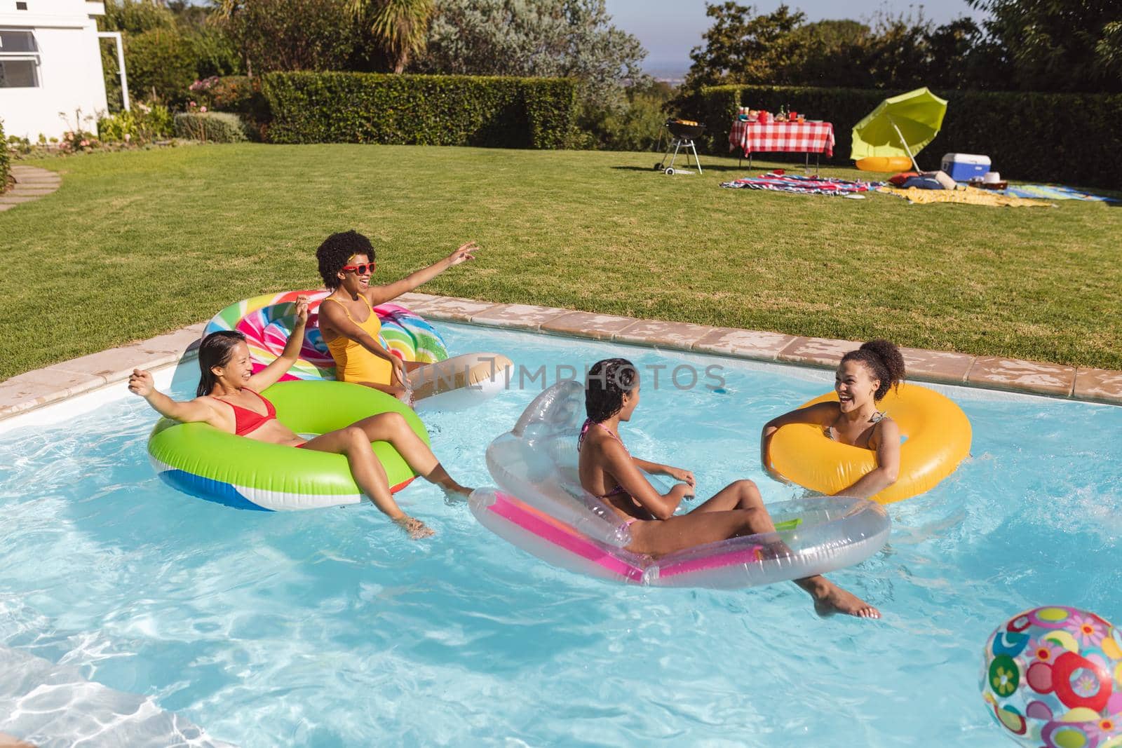 Diverse group of female friends having fun playing on inflatables in swimming pool. Hanging out and relaxing outdoors in summer.