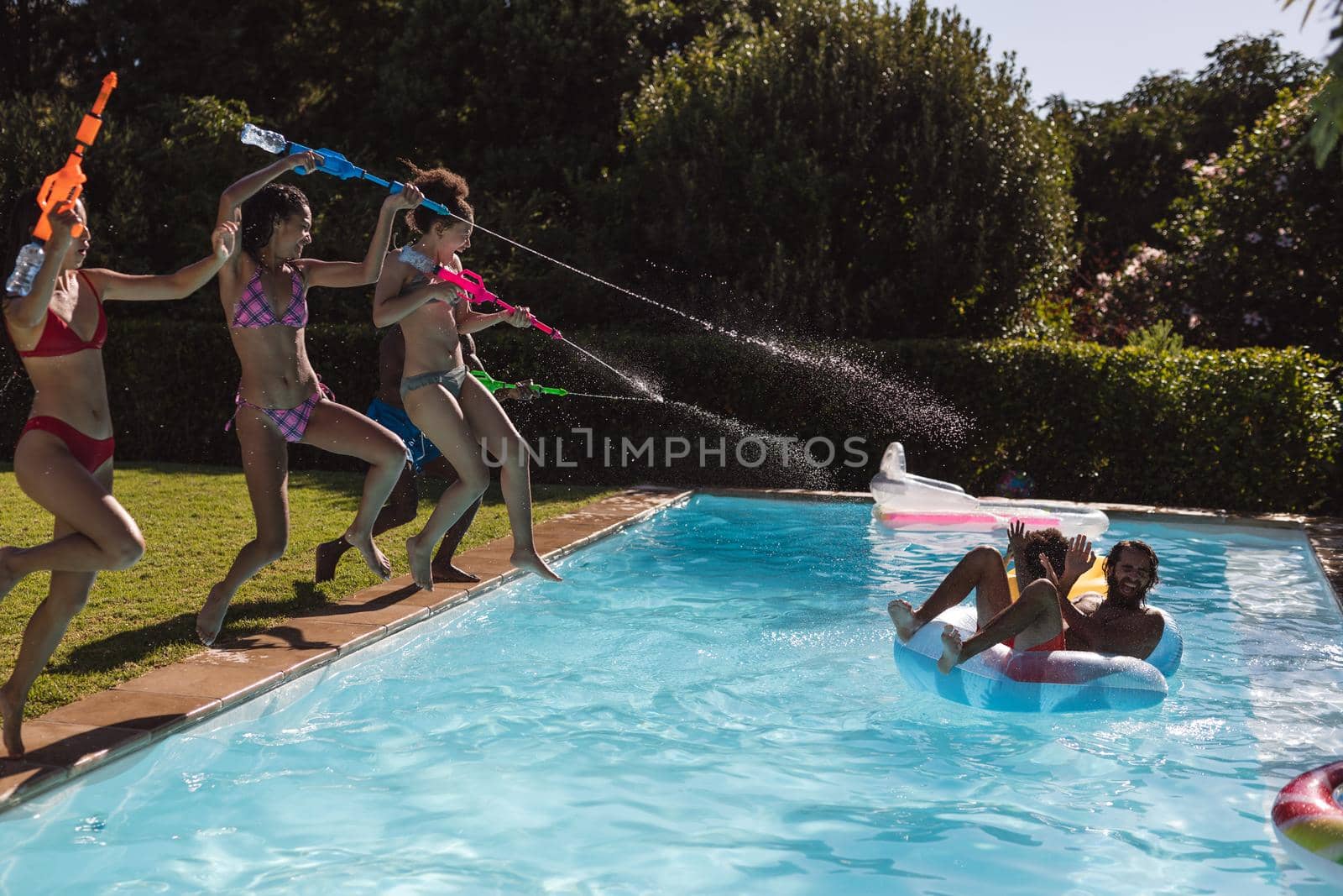 Diverse group of friends having fun playing with water guns at a pool party by Wavebreakmedia