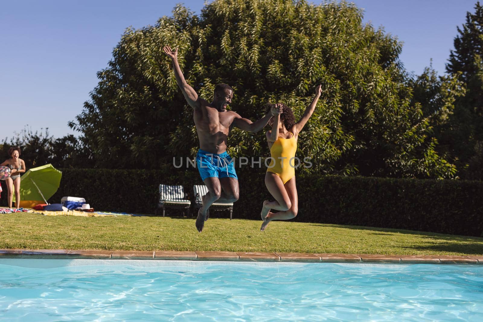 Two diverse male and female friends having fun and jumping into swimming pool. Hanging out and relaxing outdoors in summer.