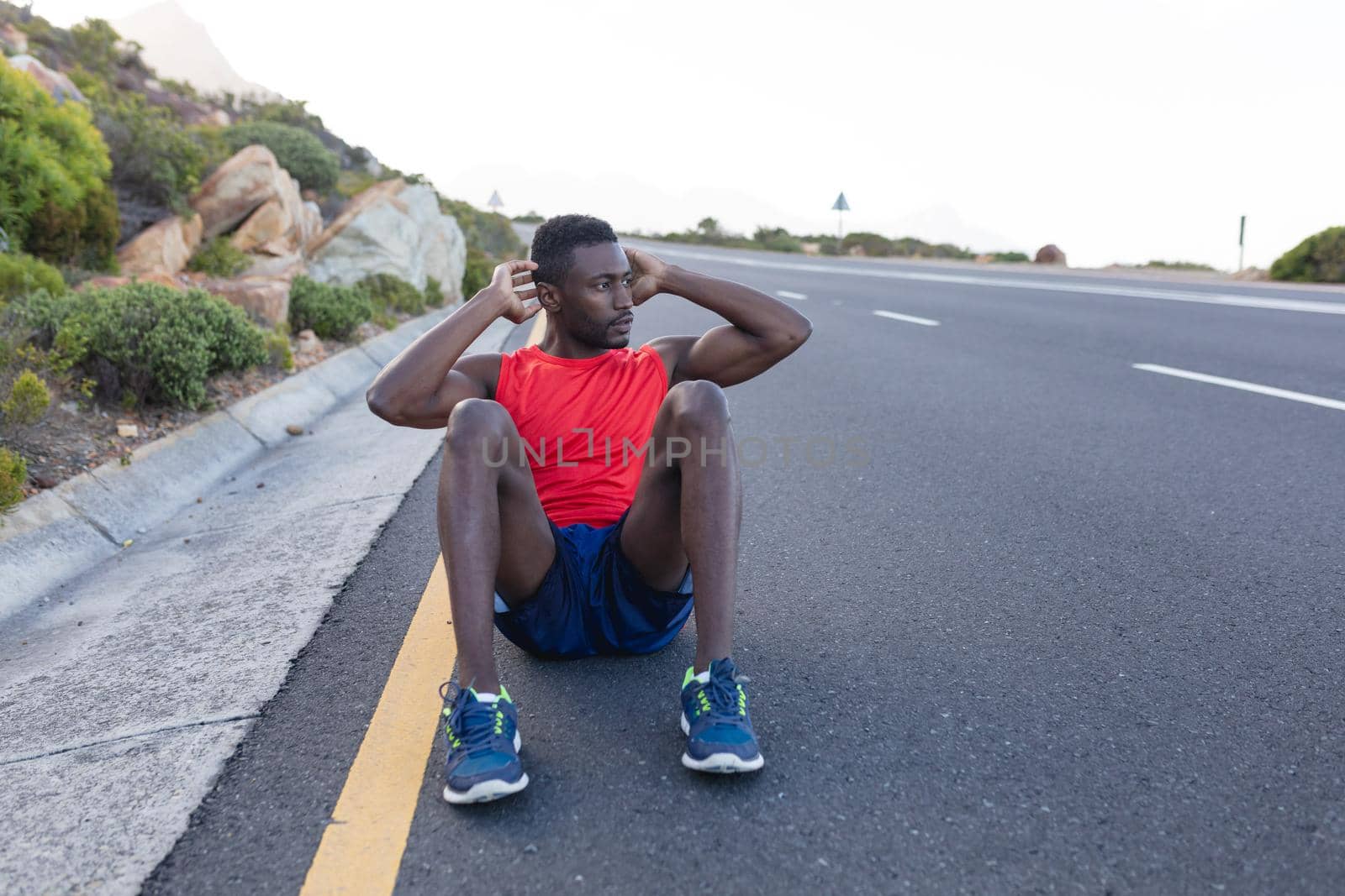 Fit african american man in sportswear doing crunches on a coastal road. healthy lifestyle, exercising in nature.