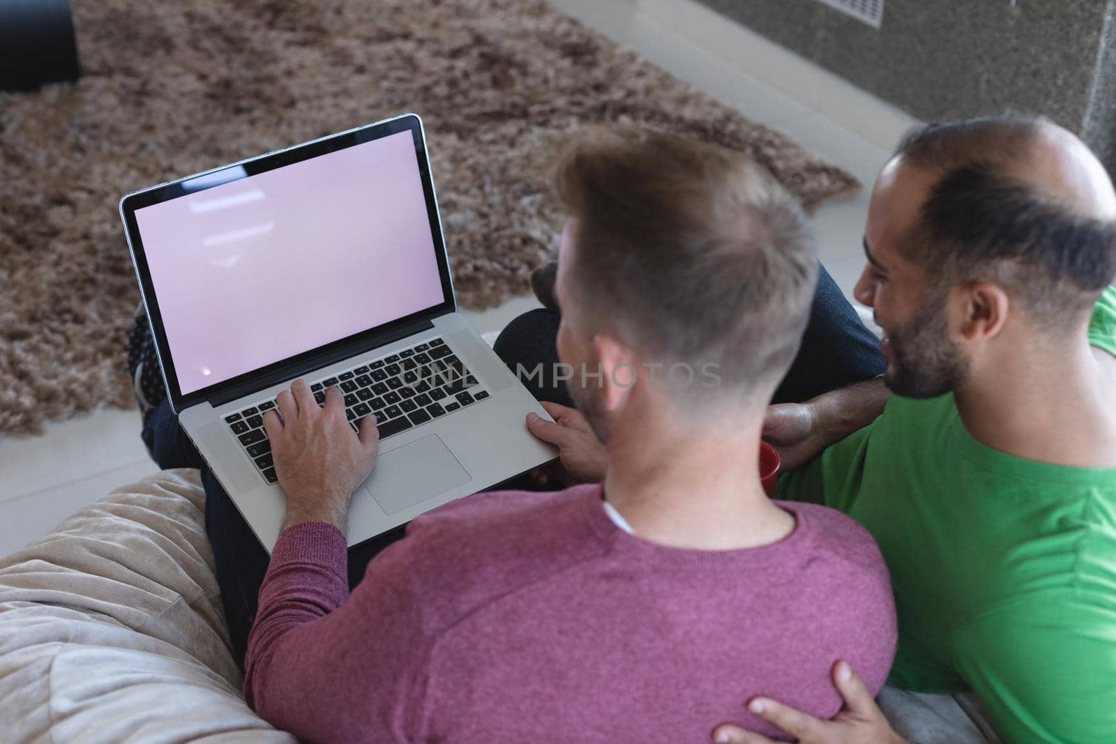 Multi ethnic gay male couple sitting on couch using laptop with copy space on screen at home. enjoying time staying at home in self isolation during quarantine lockdown.
