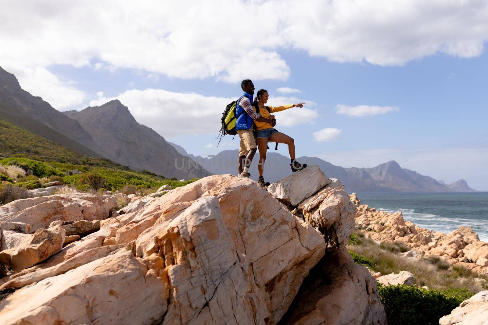 Fit afrcan american couple wearing backpacks hiking embracing on the coast. healthy lifestyle, exercising in nature.