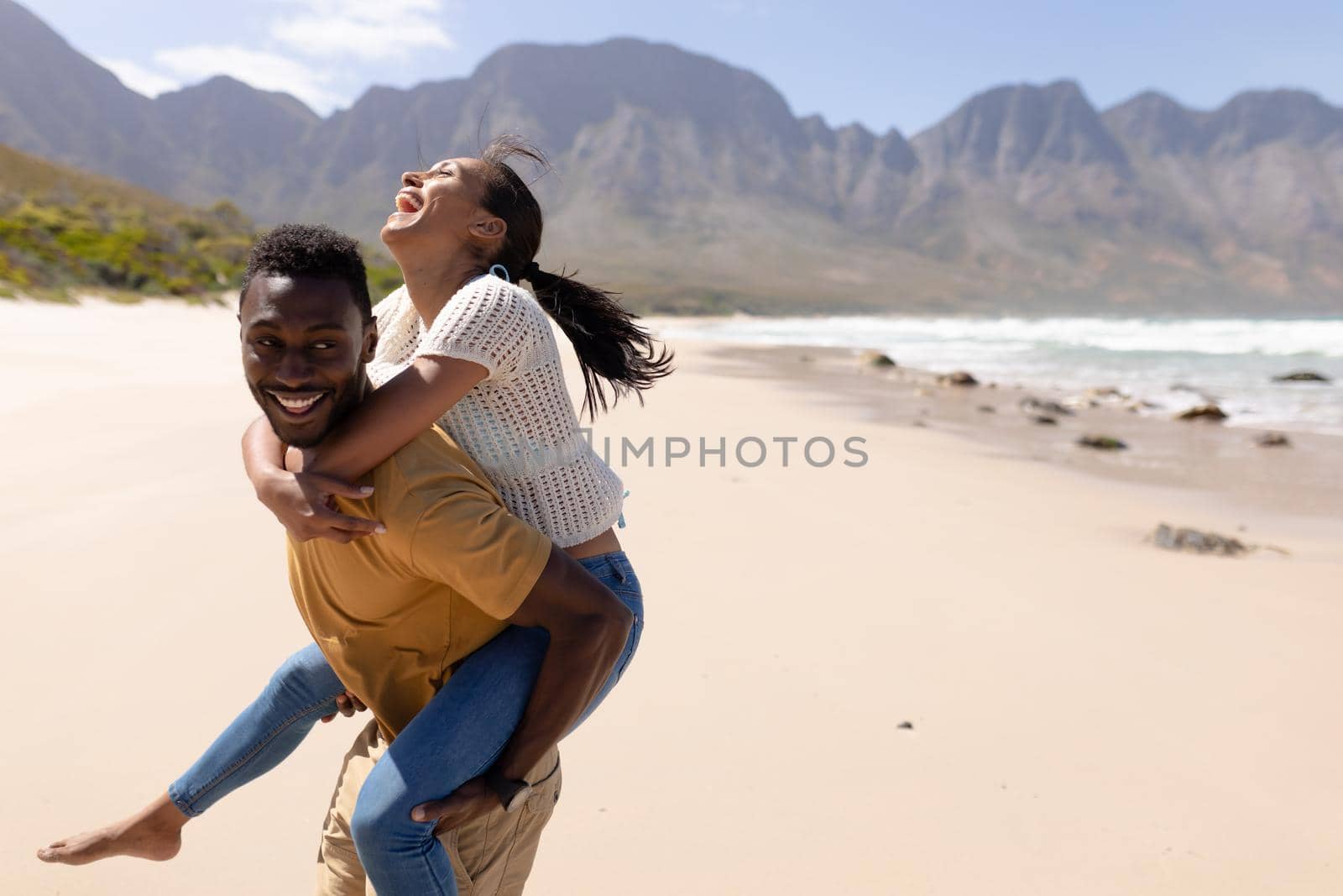 African american couple having fun piggybacking on a beach by the sea. healthy lifestyle, leisure in nature.