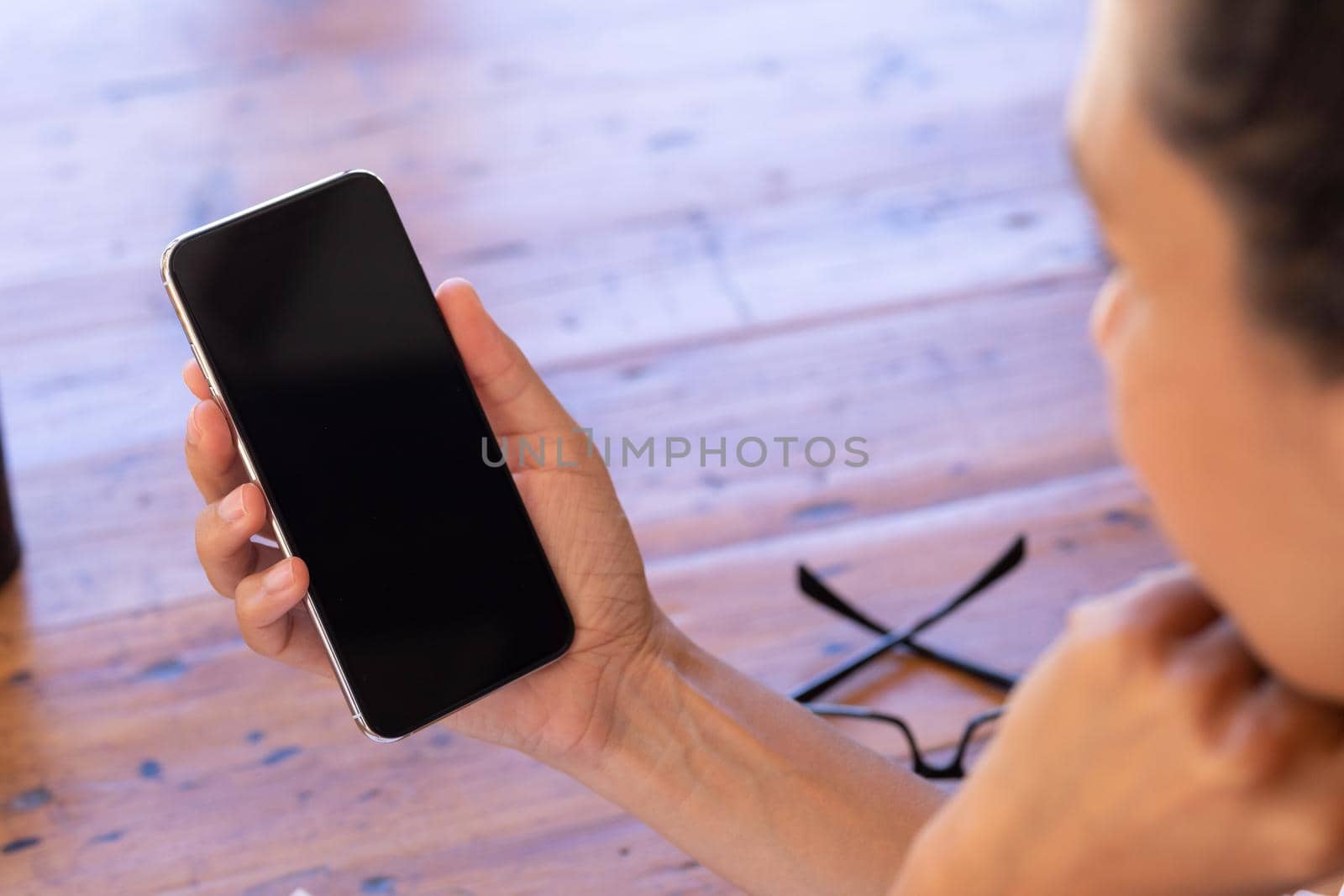 Caucasian woman using smartphone sitting by table at home. Staying at home in self isolation during quarantine lockdown.