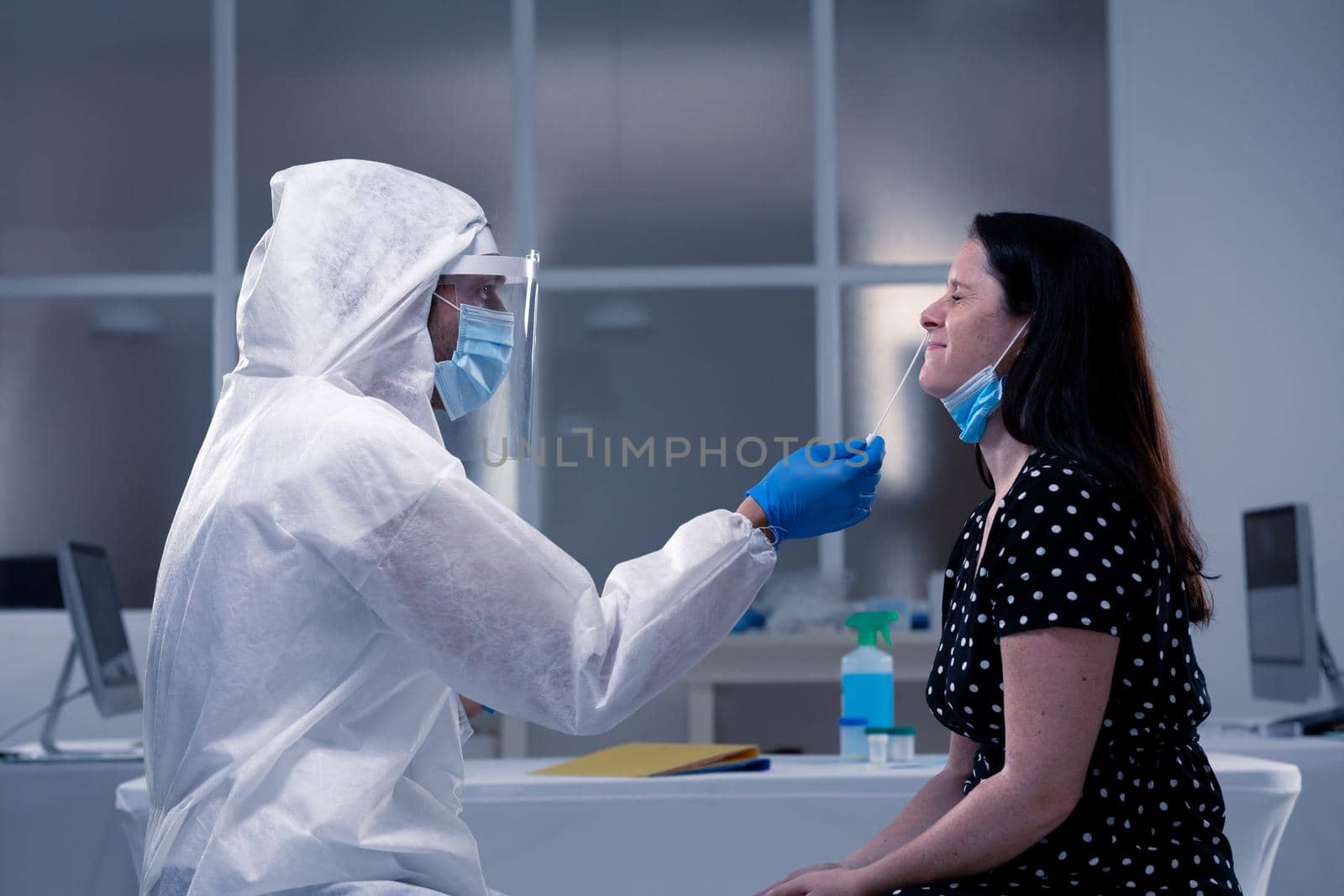 Caucasian male medical worker wearing protective clothing taking swab of masked female patient. healthcare, medical research technology and hygiene during coronavirus covid 19 pandemic.