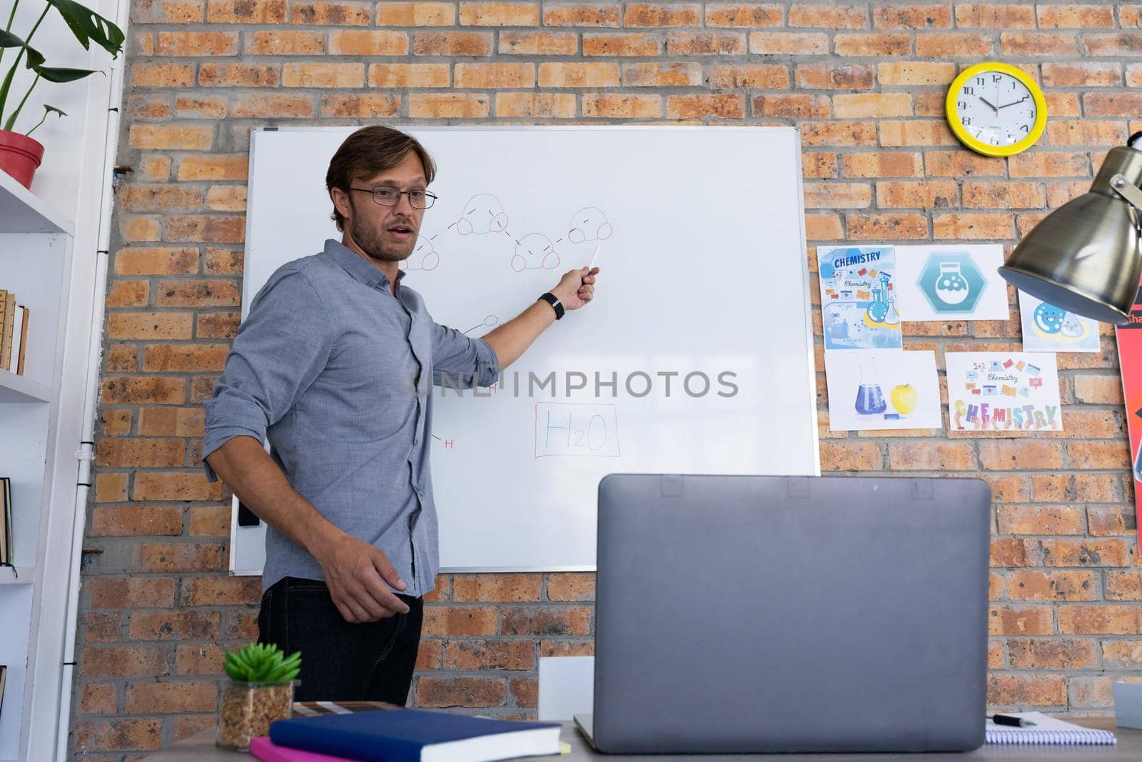 Caucasian male teacher giving online lesson using laptop standing talking at whiteboard. home schooling and online education during quarantine lockdown.
