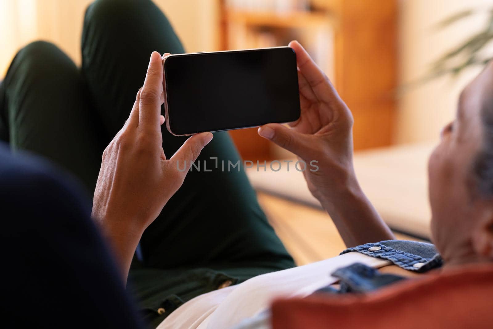 Caucasian woman using smartphone lying on sofa at home. Staying at home in self isolation during quarantine lockdown.