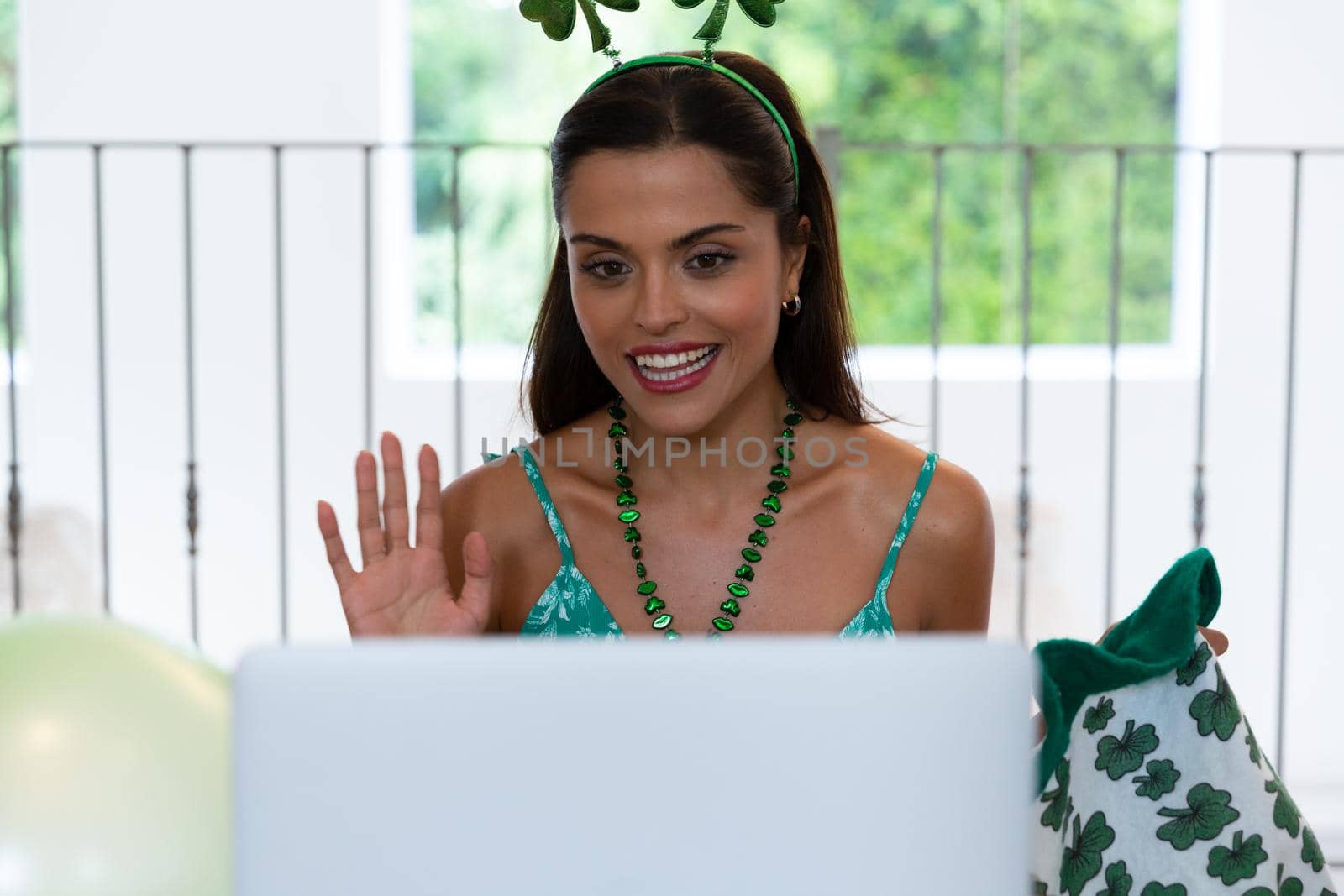 Smiling caucasian woman celebrating st patrick's day making video call and waving. staying at home in isolation during quarantine lockdown.