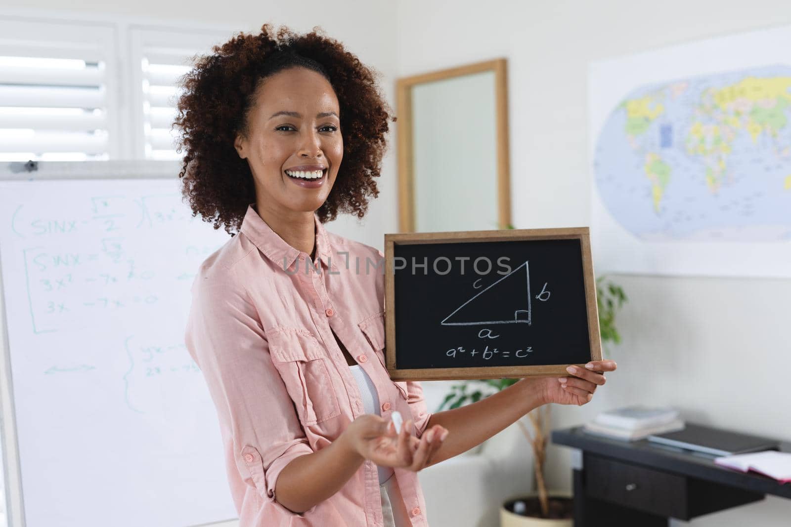 Mixed race female teacher standing at a whiteboard giving an online lesson to camera. education at home in self isolation during quarantine lockdown.