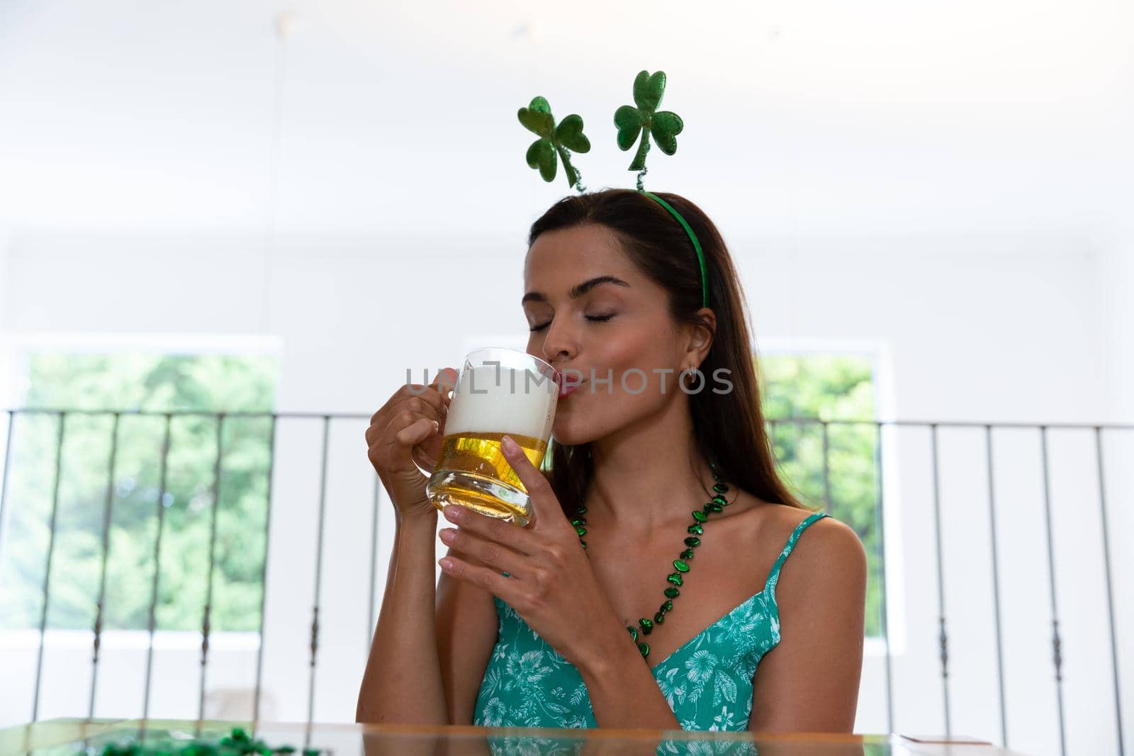 Caucasian woman celebrating st patrick's day making video call wearing deely boppers drinking beer. staying at home in isolation during quarantine lockdown.