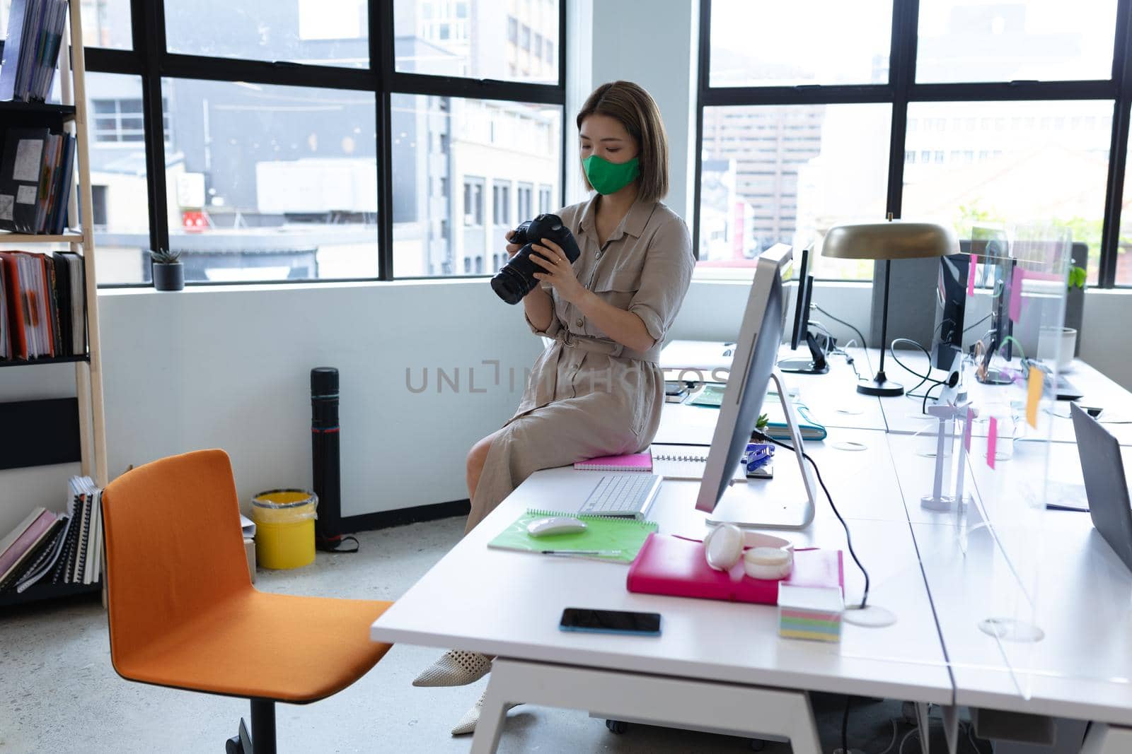 Asian businesswoman wearing face mask using camera in creative office. social distancing protection hygiene in workplace during covid 19 pandemic.