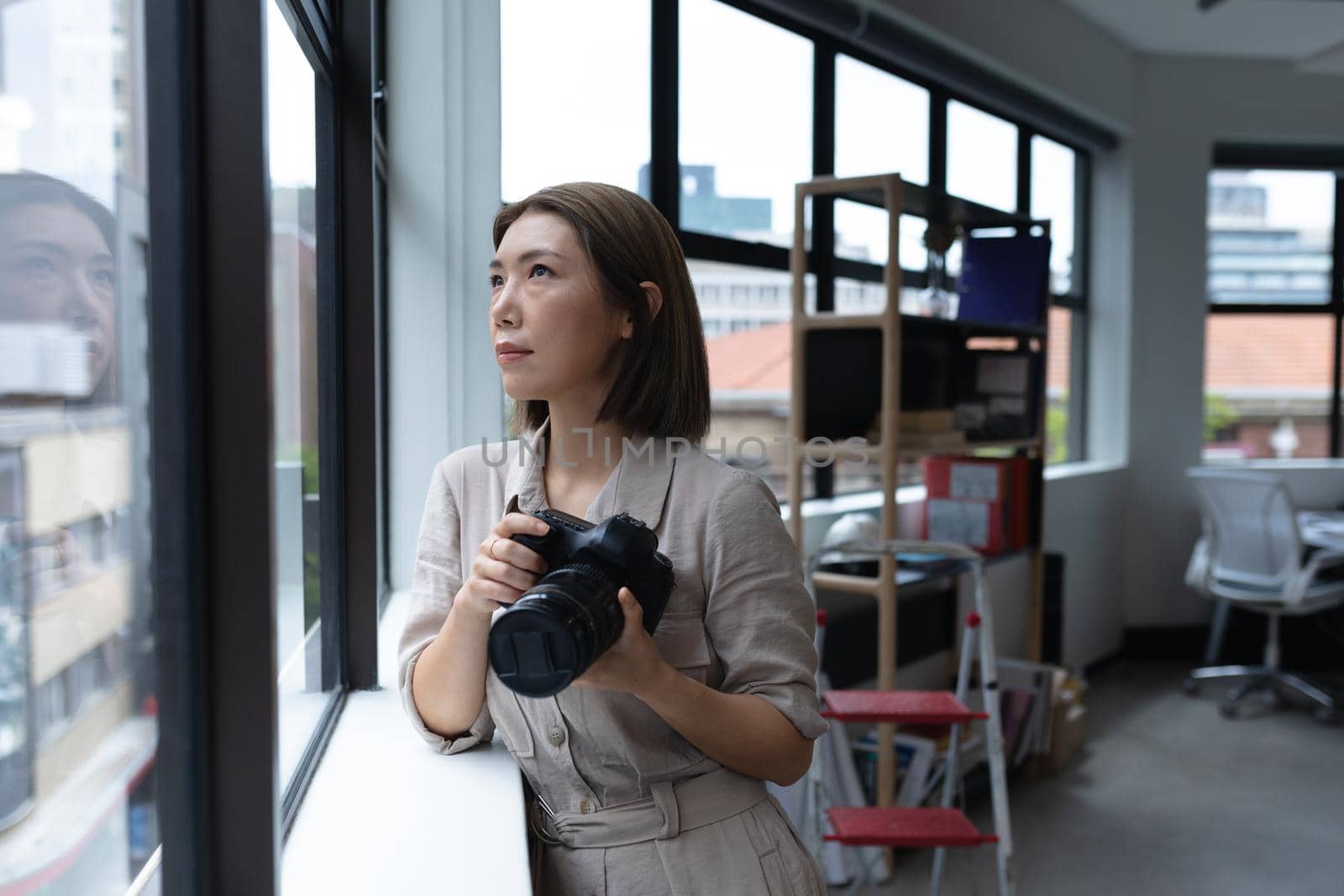 Asian businesswoman holding camera looking through window in creative office by Wavebreakmedia
