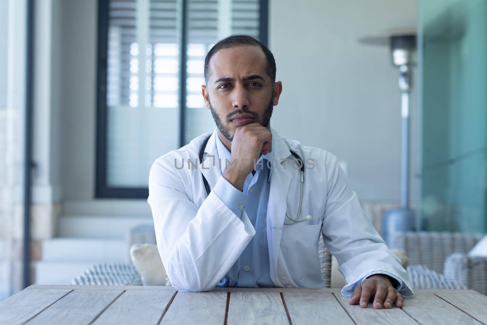 Portrait of caucasian male doctor looking at the camera and rubbing his chin. professional medical worker wearing stethoscope and lab coat.