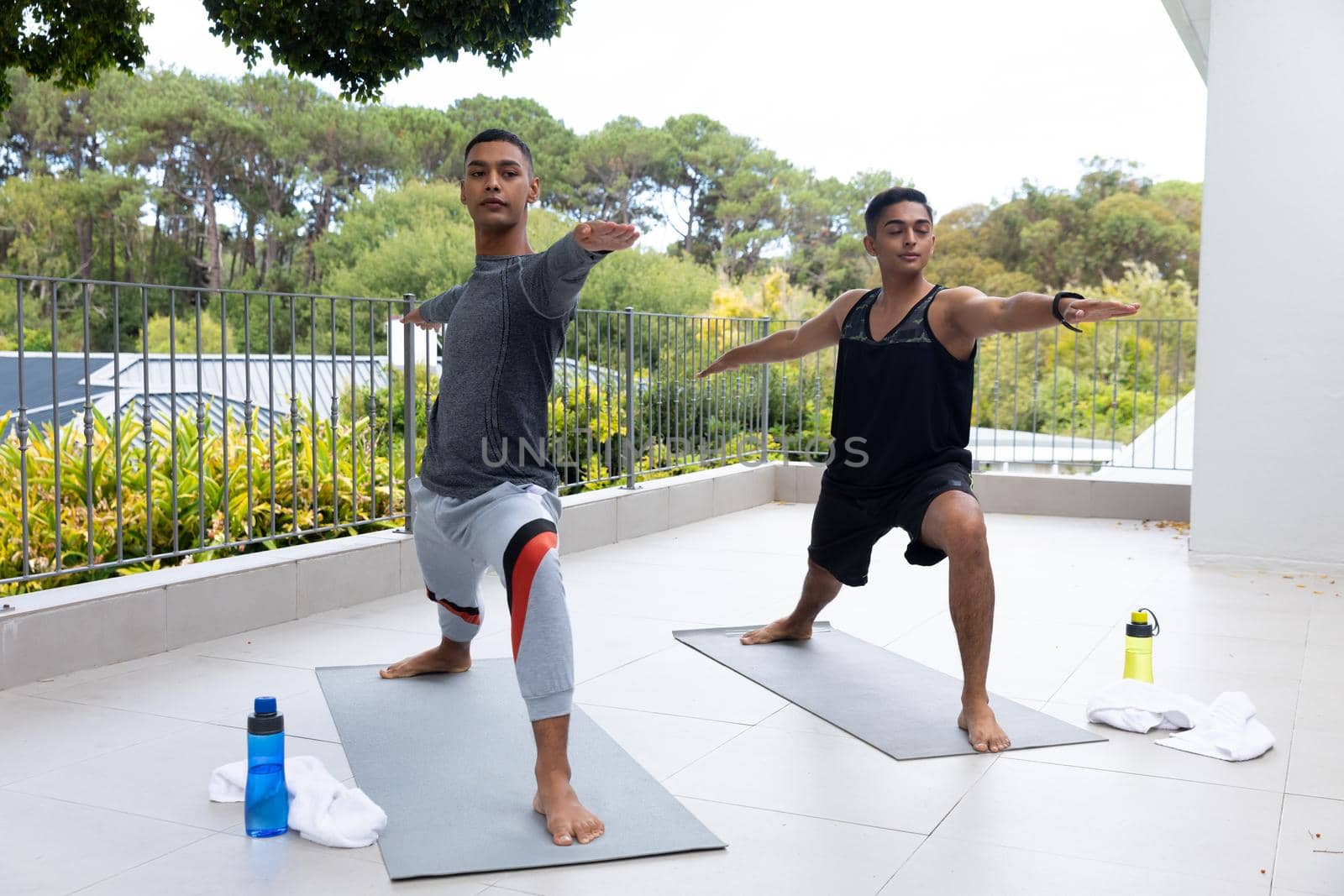 Diverse gay male couple practicing yoga on balcony. staying at home in isolation during quarantine lockdown.