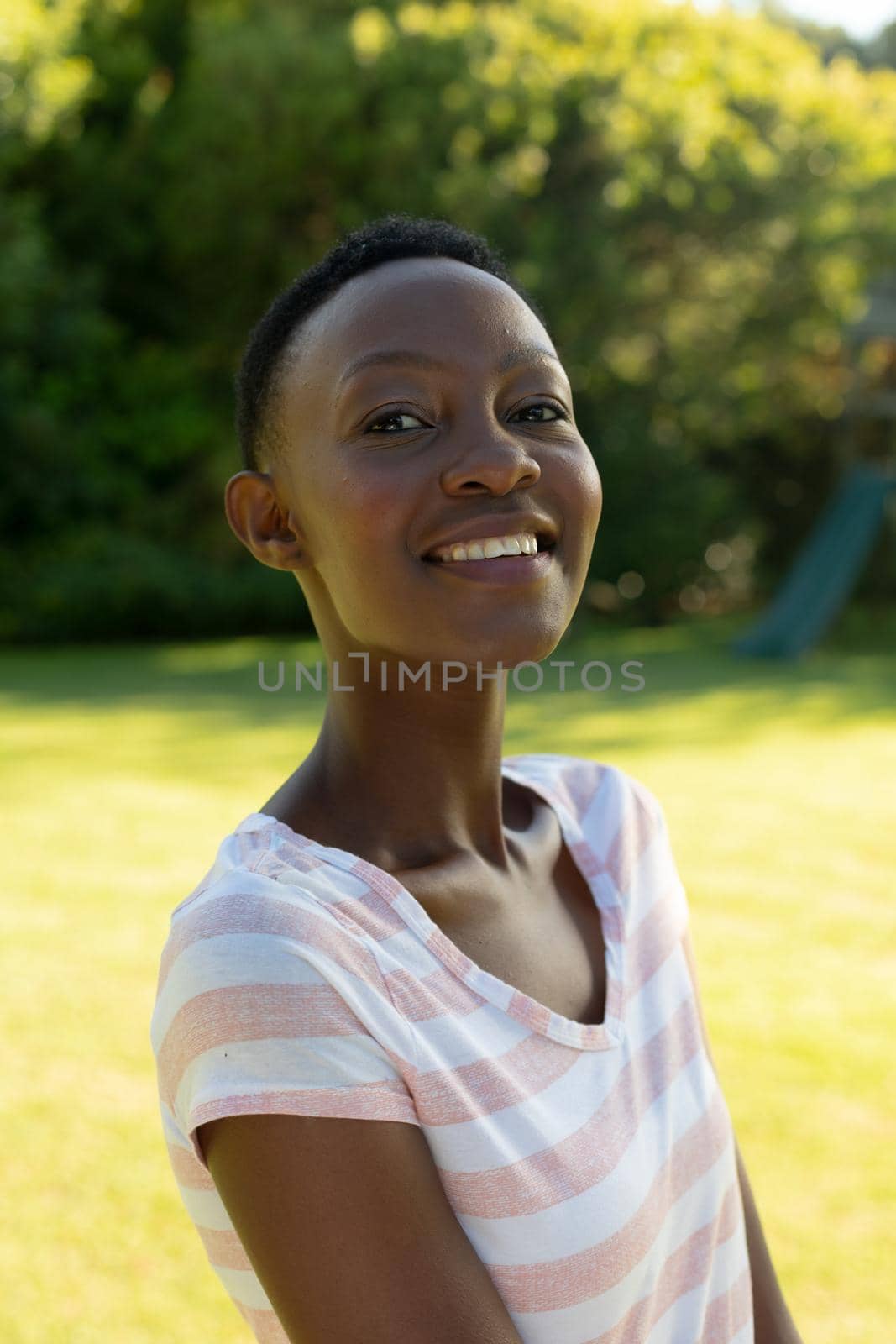 Portrait of african american woman looking at camera smiling on sunny garden terrace. staying at home in isolation during quarantine lockdown.