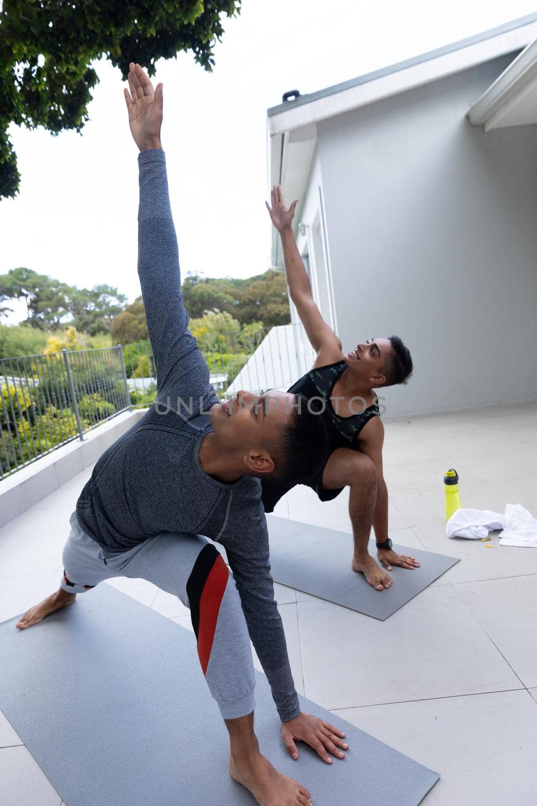 Diverse gay male couple practicing yoga on balcony. staying at home in isolation during quarantine lockdown.